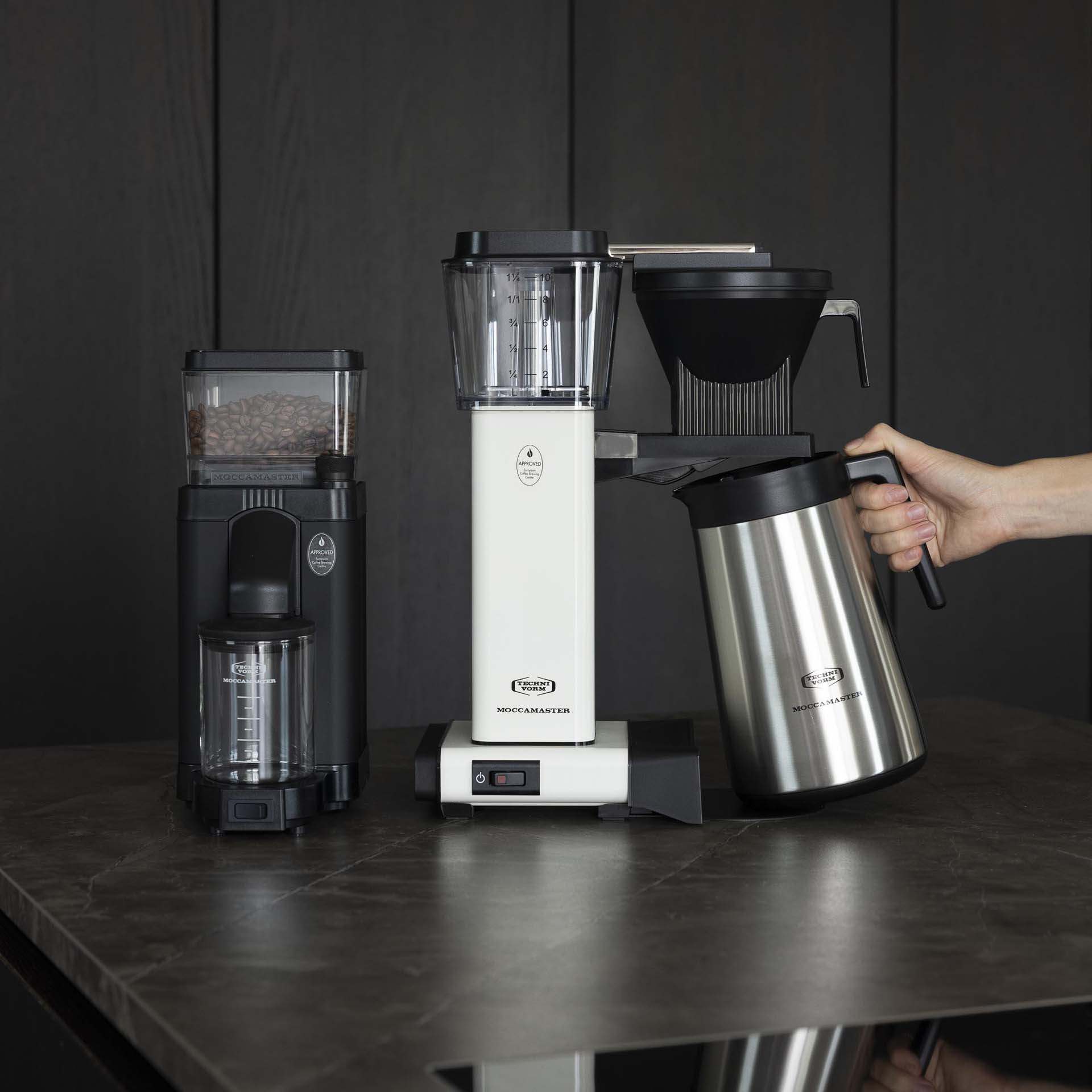 Macinacaffè, caffettiera e caraffa termica su un bancone scuro.