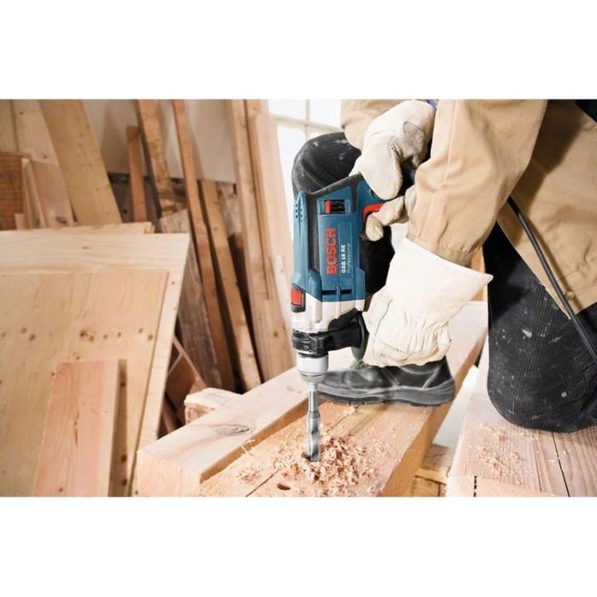 Person bohrt Holz mit blauer Bosch Bohrmaschine, Sägespäne fliegen.