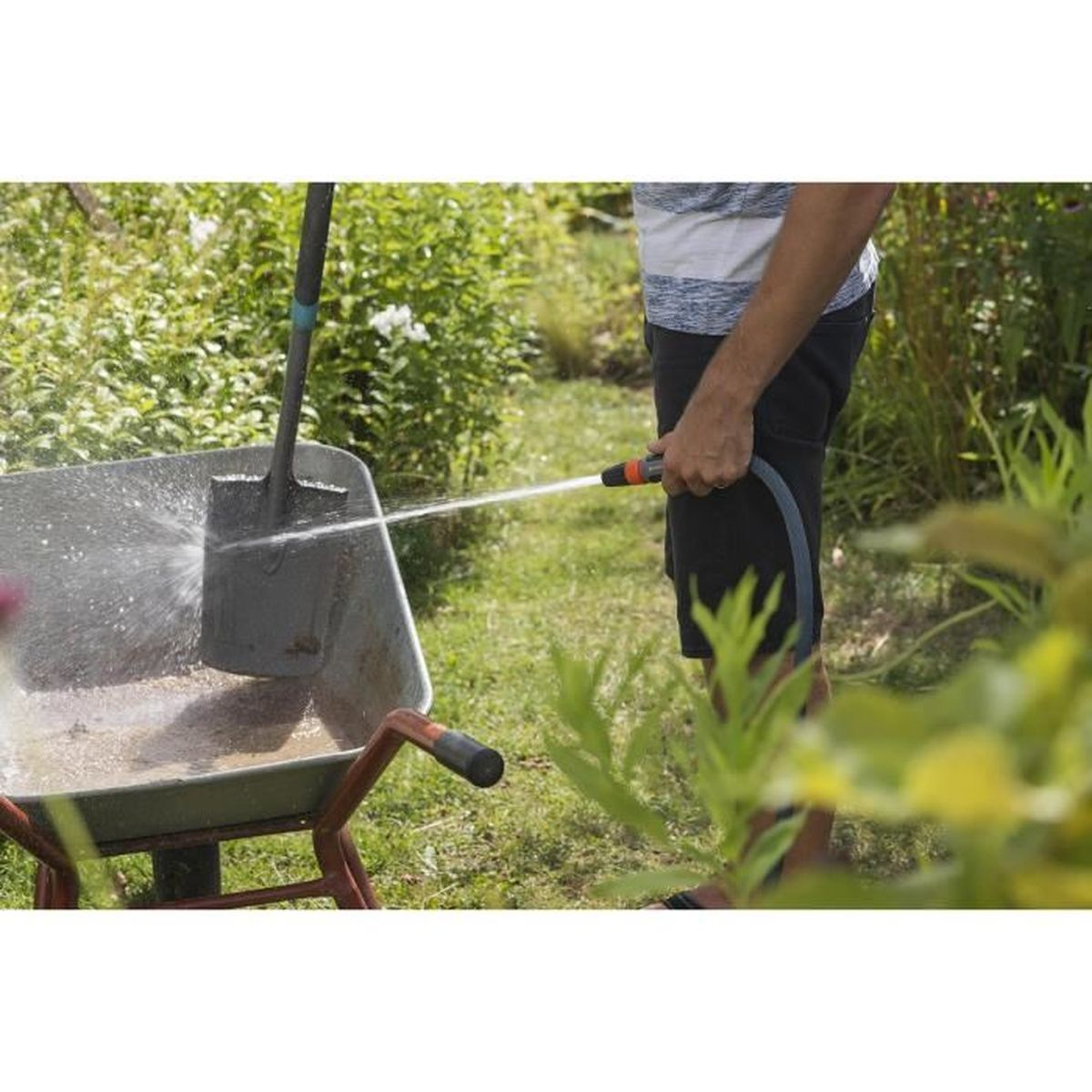 Mann spült Schaufel in einer Schubkarre mit Gartenschlauch