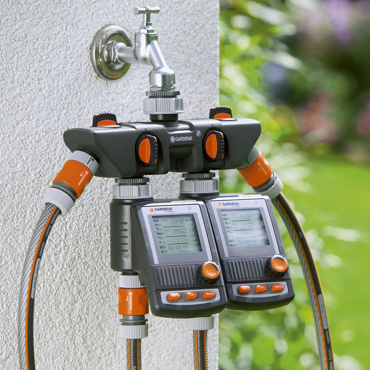 Ein schwarzer Gardena-Wasserverteiler mit zwei digitalen Timern an einer Wand montiert.
