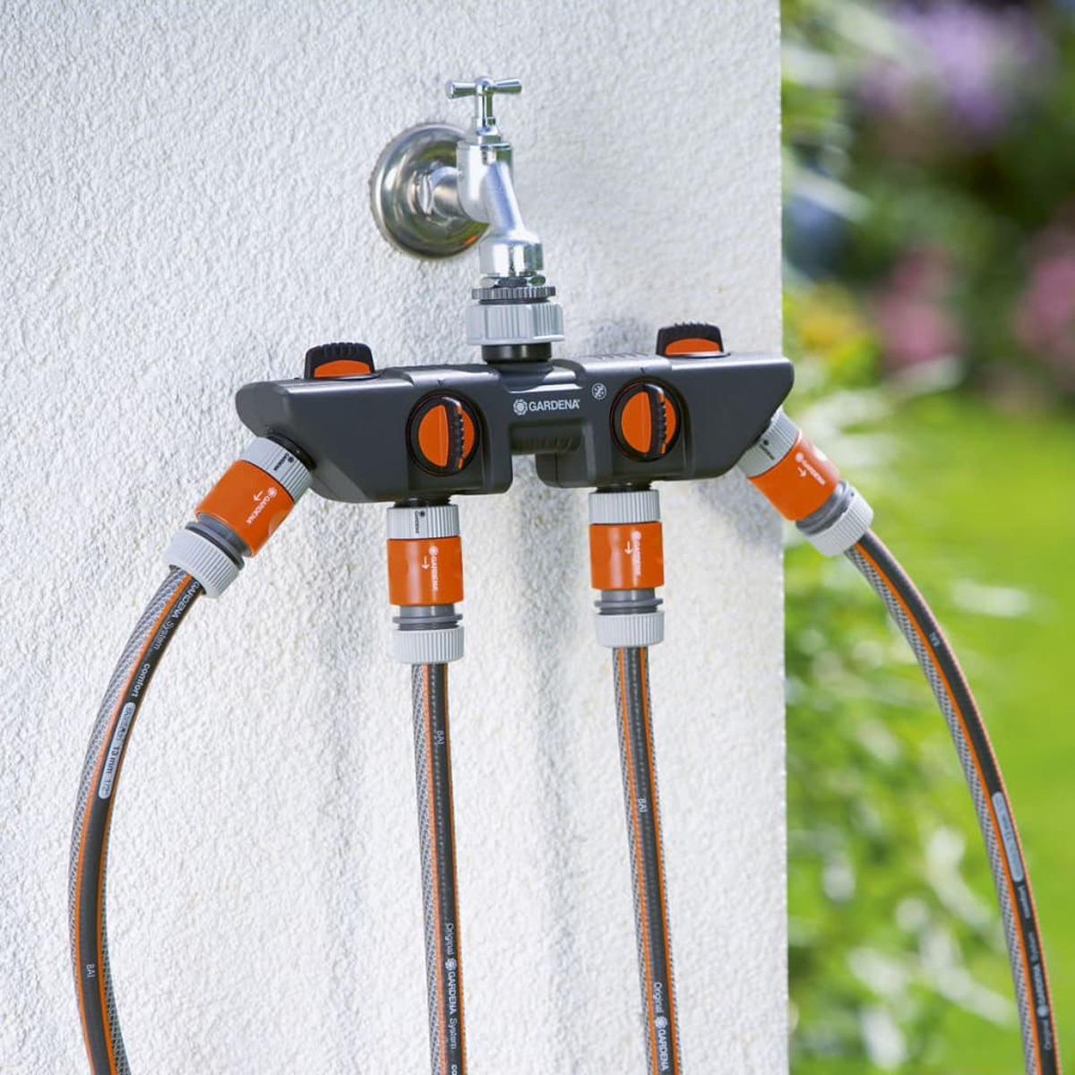 Ein Gartenwasserverteiler mit vier Anschlüssen und Schläuchen an einer Wand.