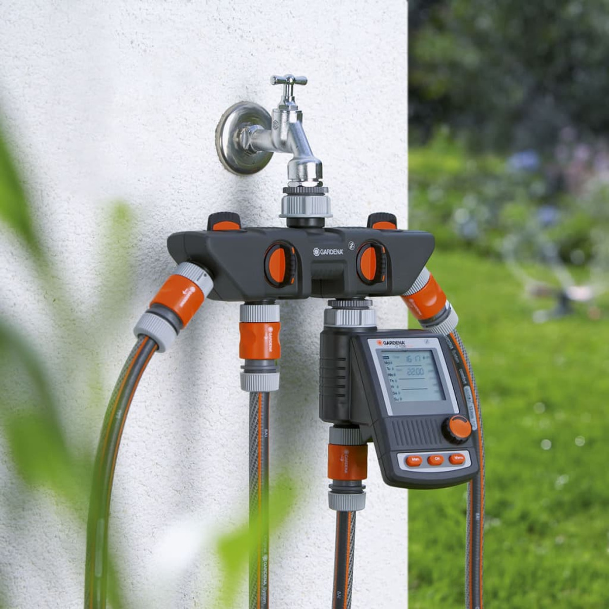 Gardena Wasserverteiler mit Zeitschaltuhr an einem Wasserhahn an einer Wand, mit angeschlossenen Schläuchen.