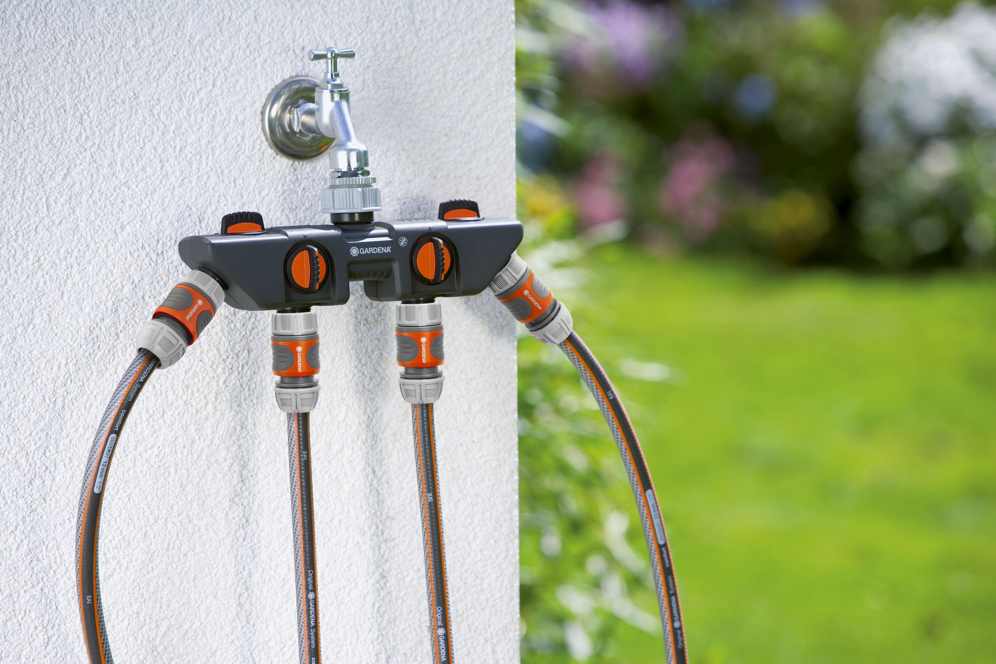 Ein grauer Gardena-Wasserverteiler mit orangefarbenen Reglern und angeschlossenen Schläuchen.