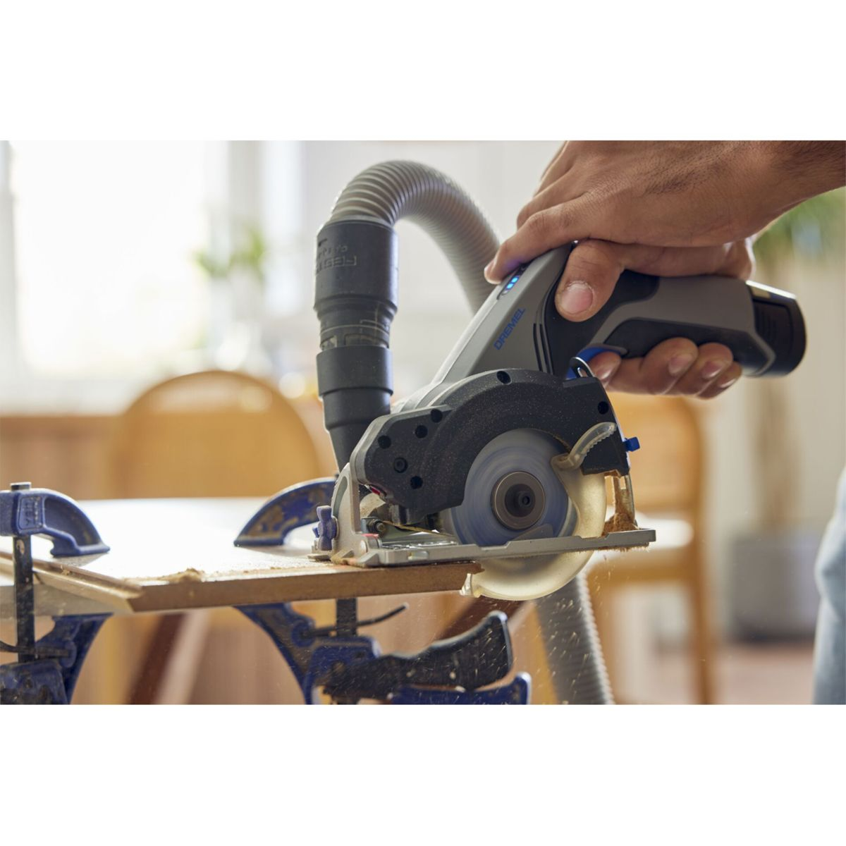 Hand hält Kreissäge, die Holz schneidet. Staub wird abgesaugt.