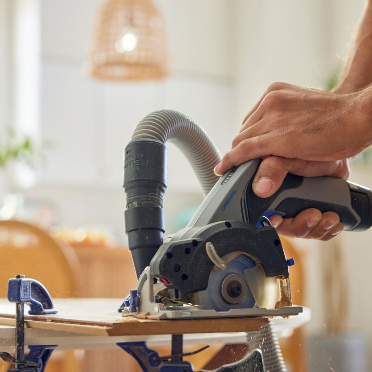 Hände bedienen eine Dremel-Kreissäge, die Holz schneidet, mit angeschlossenem Staubabsaugschlauch.