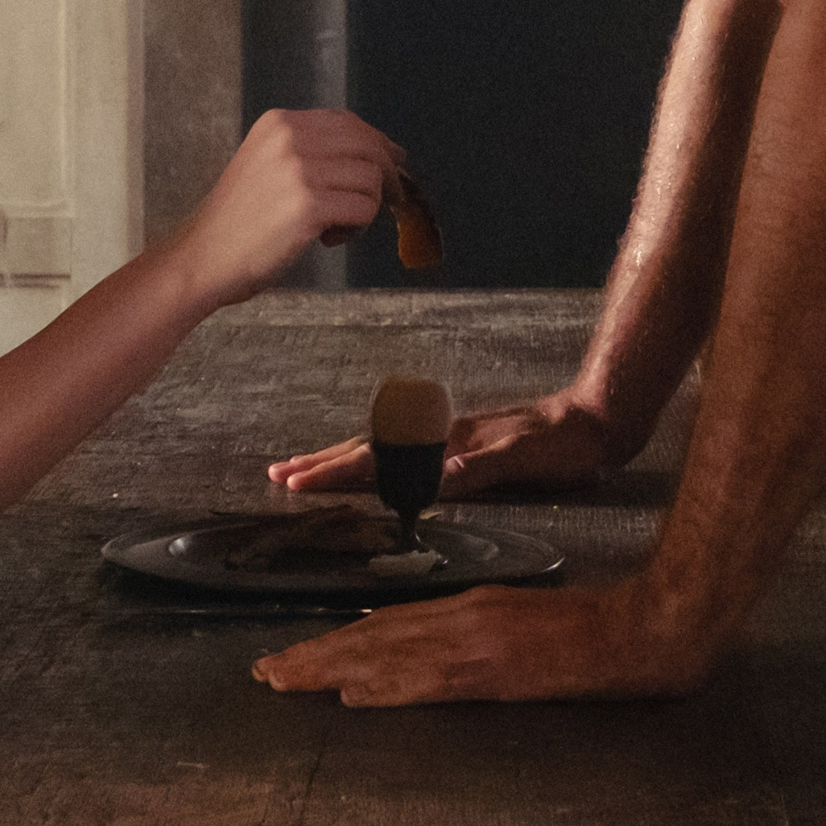 Mani tengono cibo sopra un tavolo con un bicchiere e un piatto piccoli.
