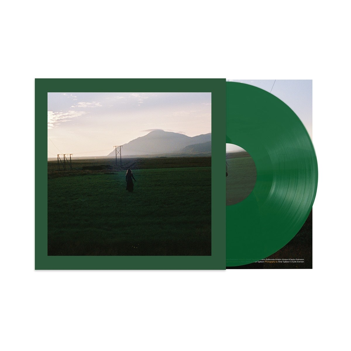Disco in vinile verde accanto a copertina con donna in campo davanti montagna.