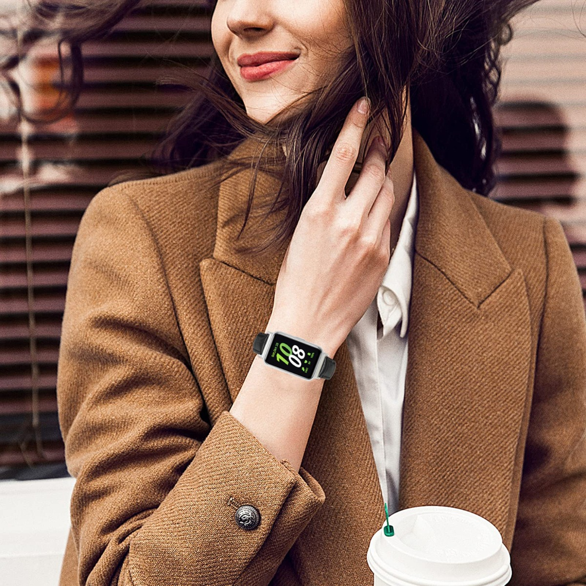 Frau mit braunem Mantel trägt eine Smartwatch, hält einen Kaffeebecher.