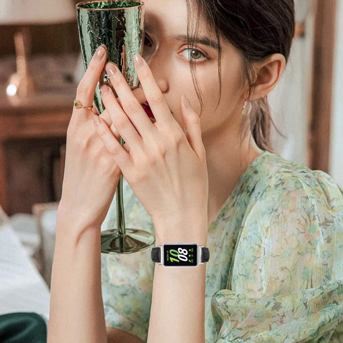 Eine Frau hält ein grünes Glas, trägt eine Uhr mit schwarzem Band.