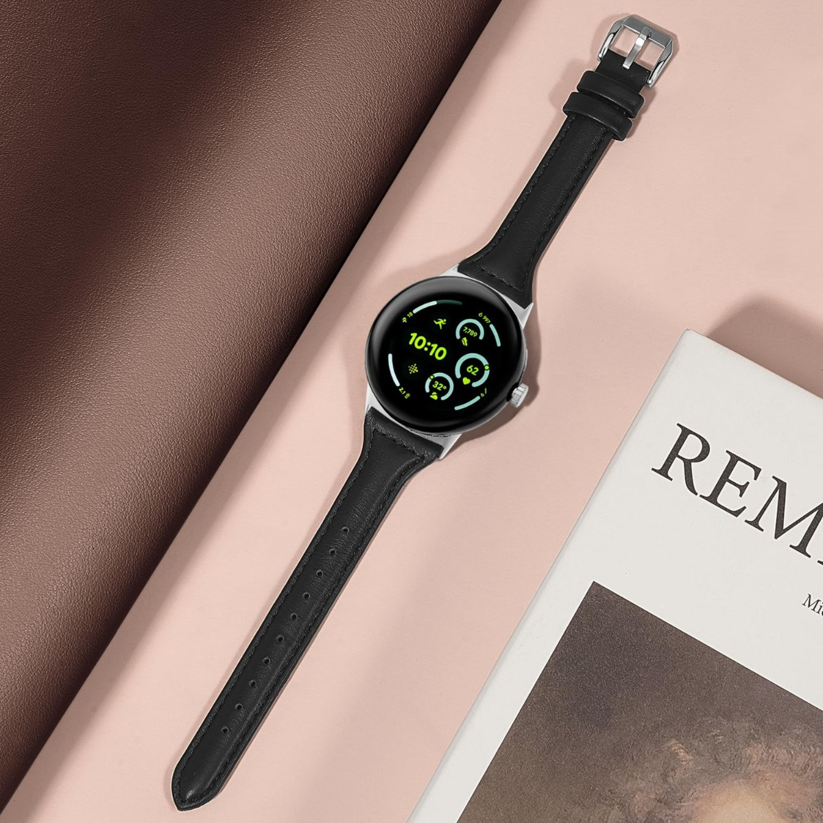 Un orologio con cinturino in pelle nera e cassa argentata su superficie rosa.