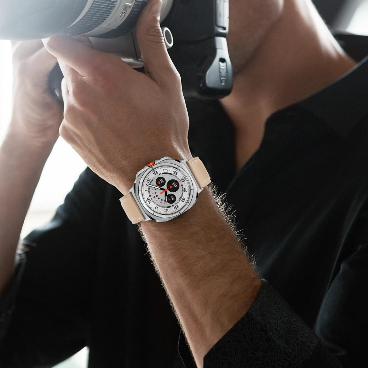 Un uomo indossa un orologio d'argento con cinturino in pelle chiara e fotocamera.