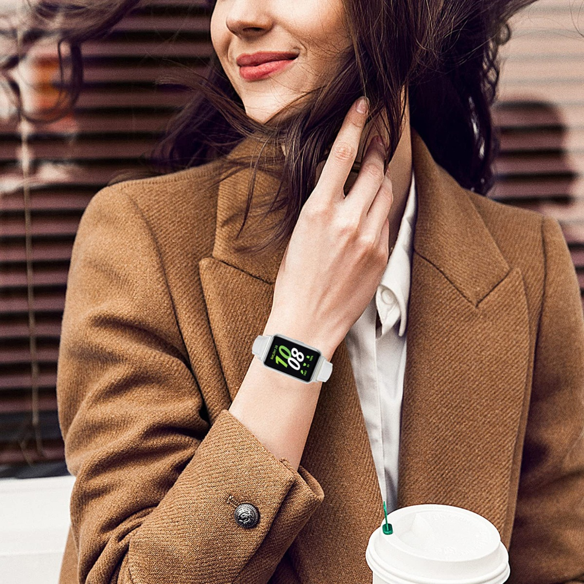 Frau mit braunem Mantel trägt eine weiße Smartwatch mit grüner Anzeige.