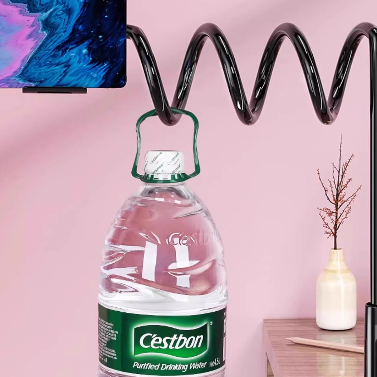 Eine Flasche Wasser hängt an einer schwarzen Spirale vor einem rosafarbenen Hintergrund.