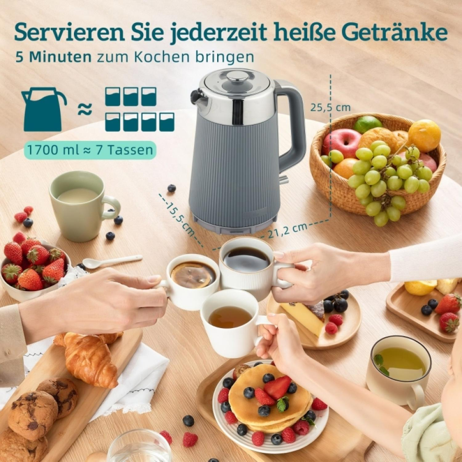 Grauer Wasserkocher mit Früchten und Gebäck auf einem Holztisch.