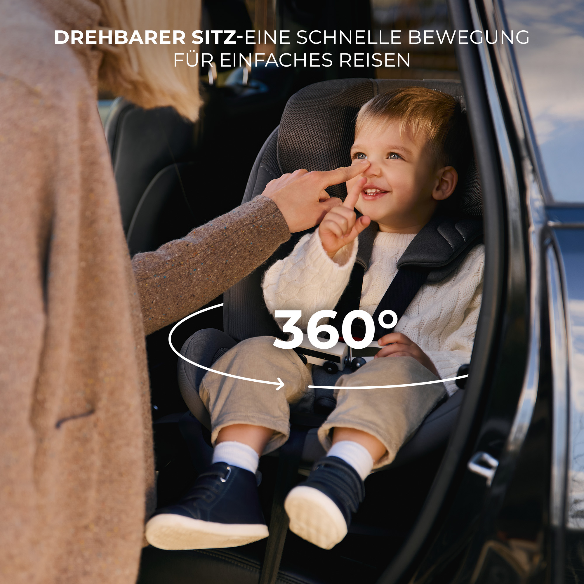 Ein Kind sitzt in einem drehbaren Autositz, eine Hand berührt seine Nase.