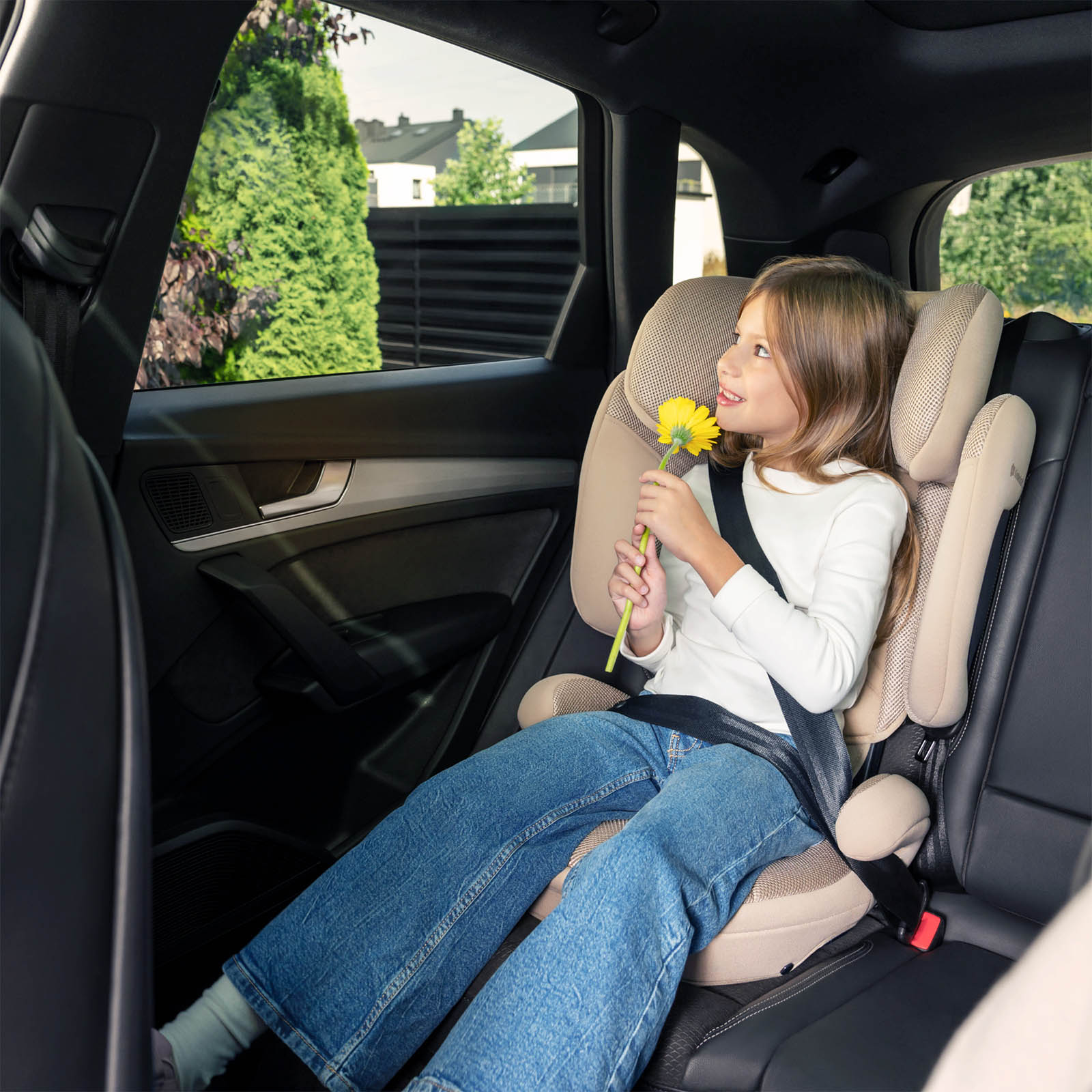 Ein Mädchen im Kindersitz hält eine gelbe Blume in einem Auto.