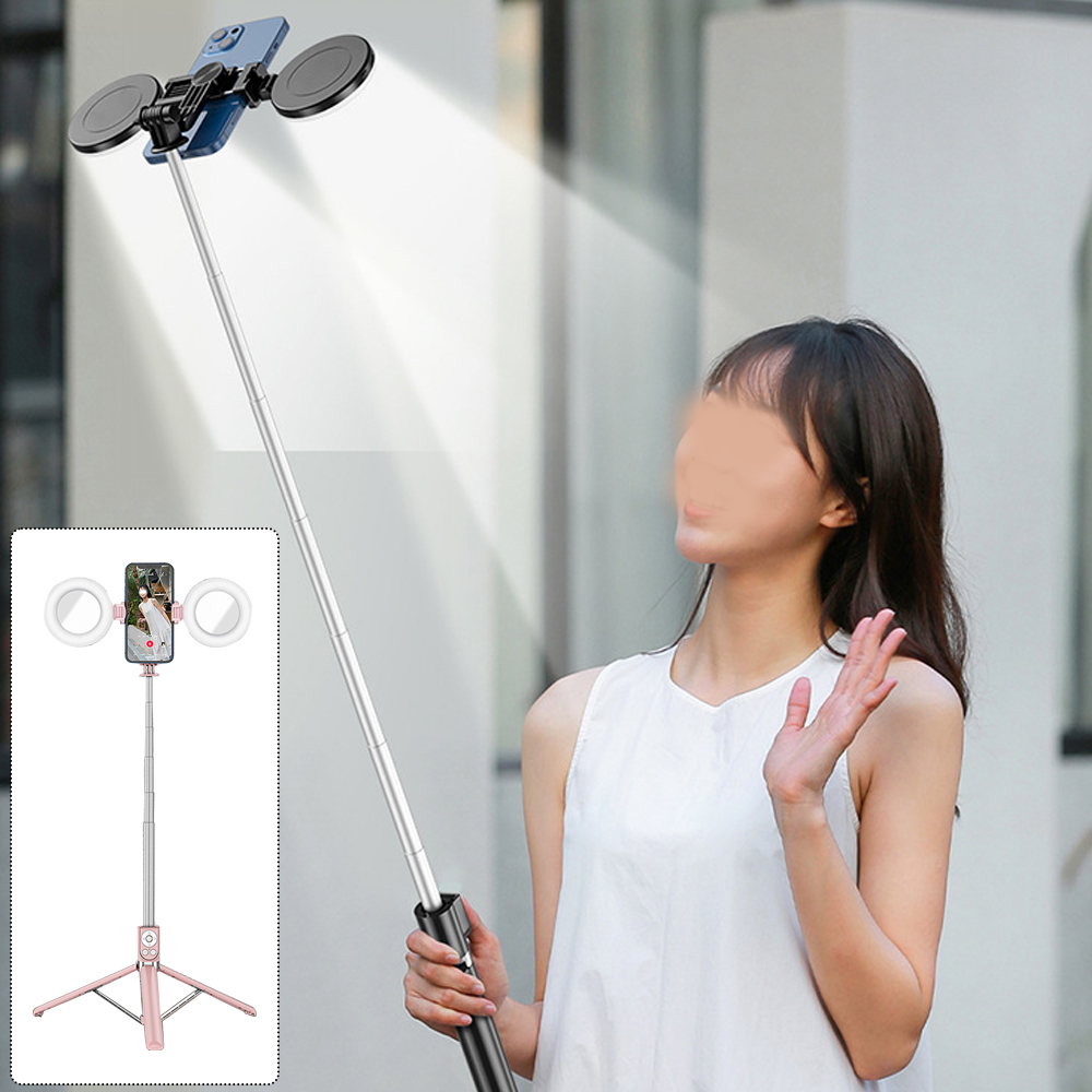 Ein Selfie-Stick mit zwei Lichtern hält ein Handy. Eine Frau winkt im Hintergrund.