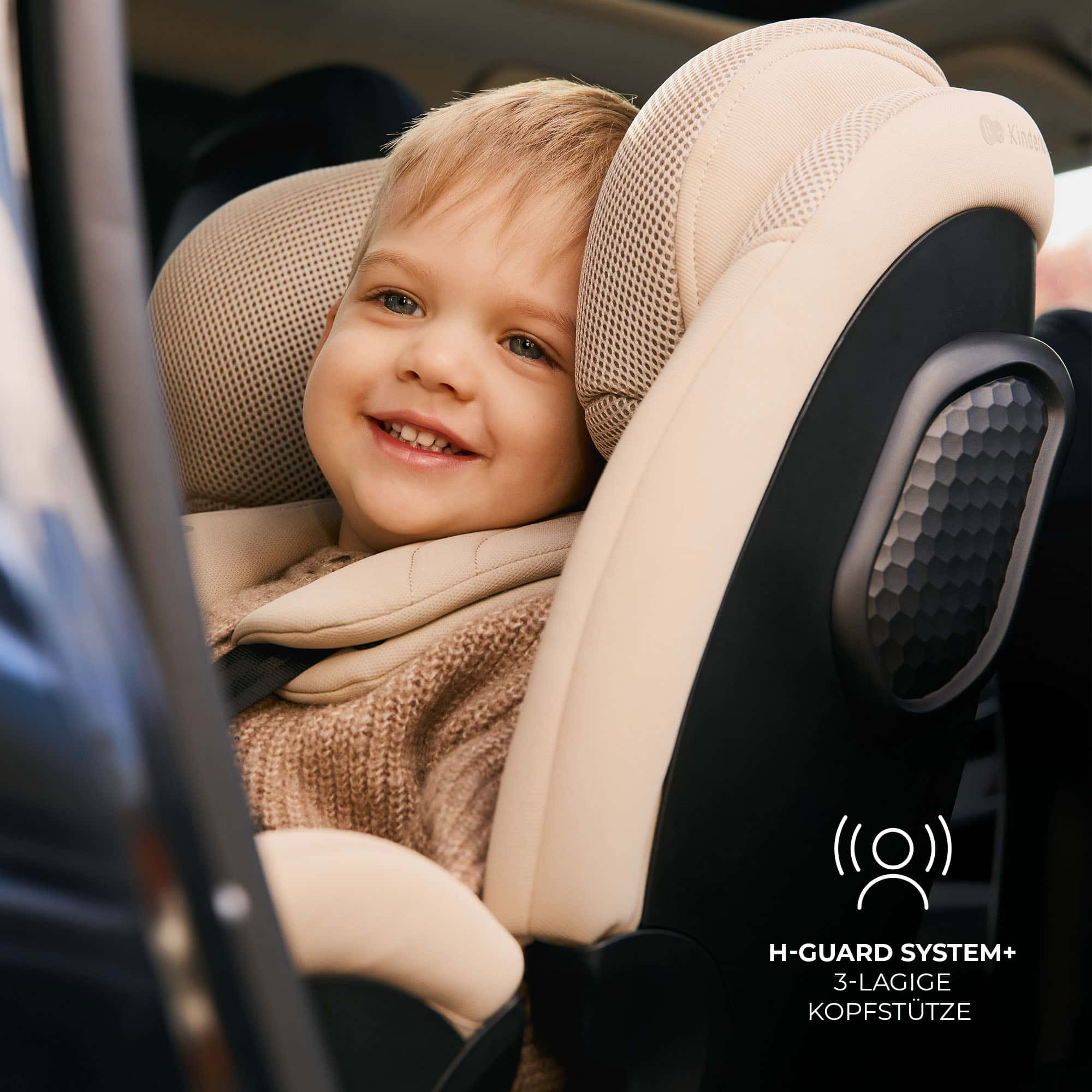 Ein lächelndes Kind sitzt in einem beigen Kindersitz im Auto.