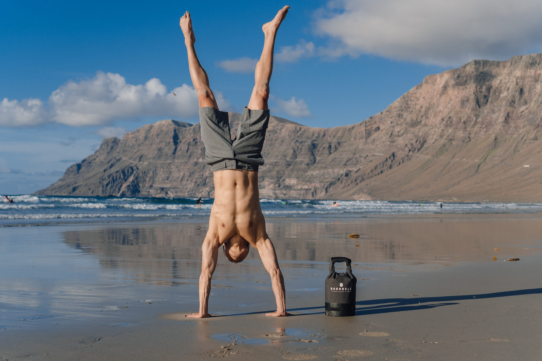 Homme en équilibre sur les mains sur la plage, montagne et sac.