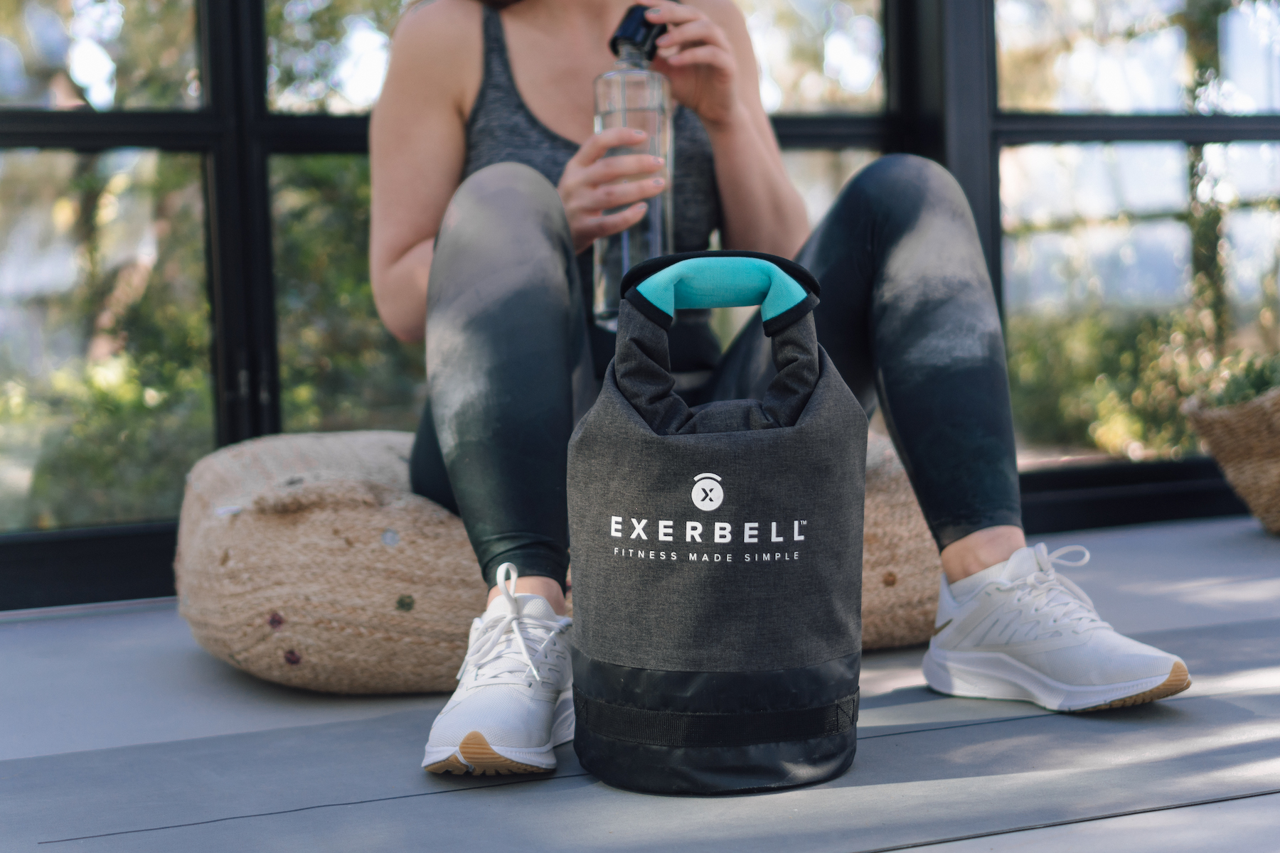 Une personne assise sur un coussin à côté d'un sac de sport boit de l'eau.