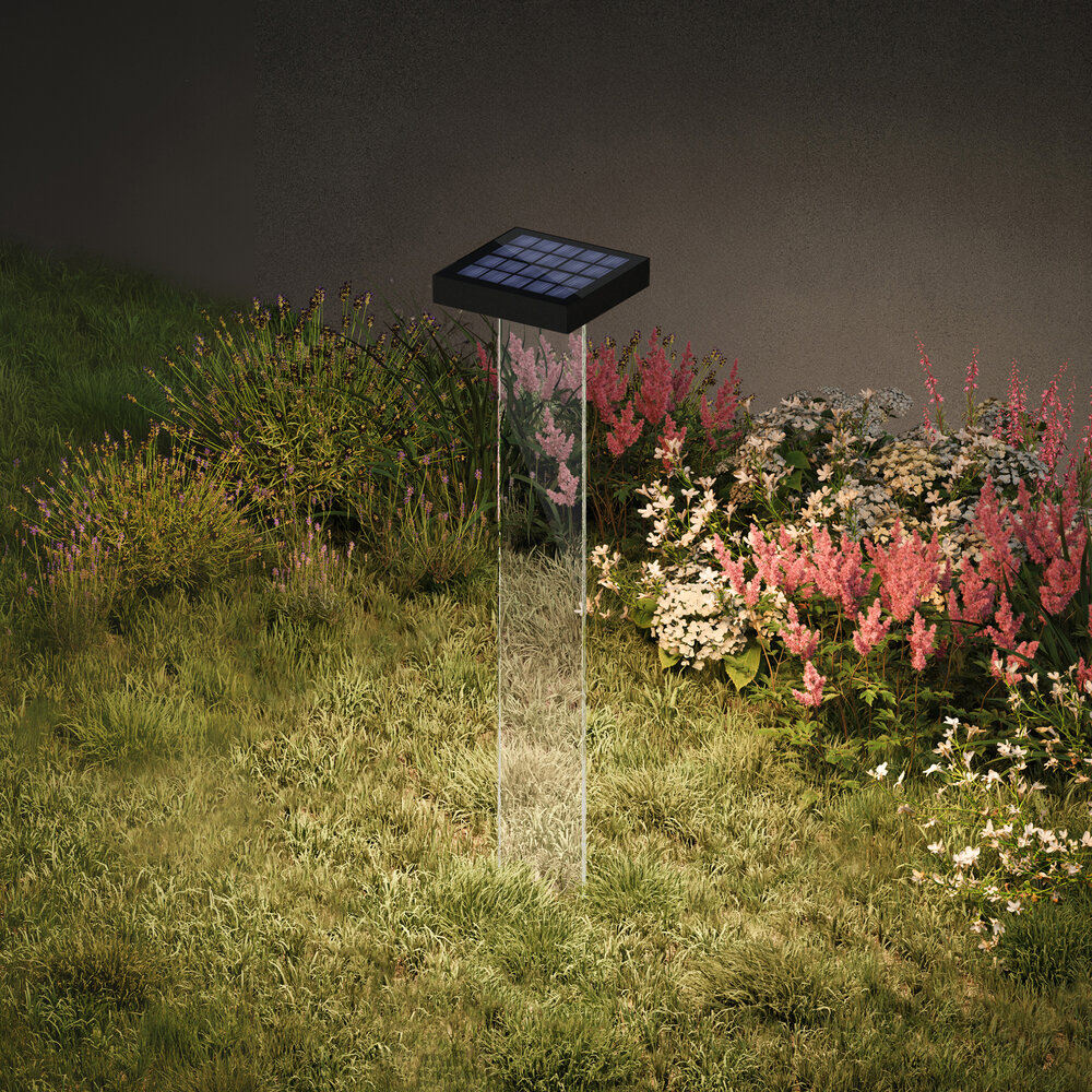 Ein solarbetriebener Gartenlichtpfosten mit transparentem Schaft steht in einem Blumenbeet.