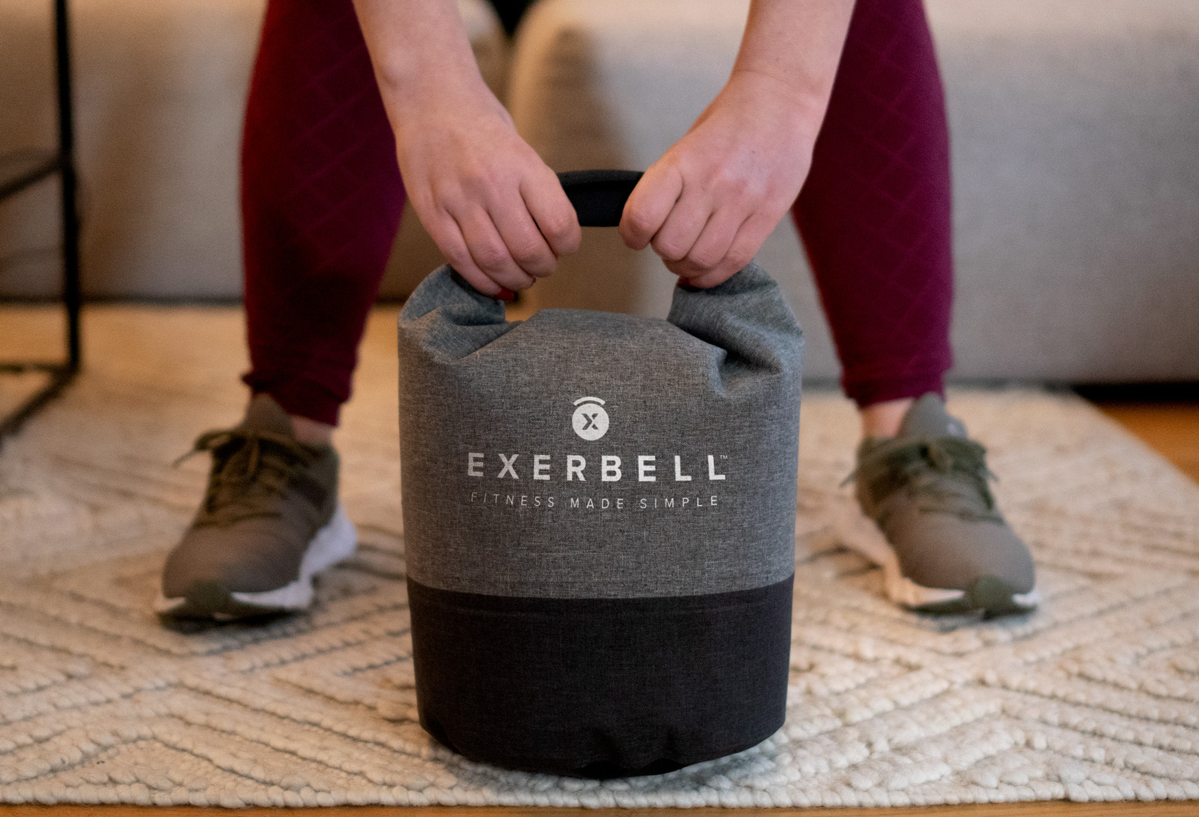 Kettlebell en tissu gris avec poignée, tenu par des mains.