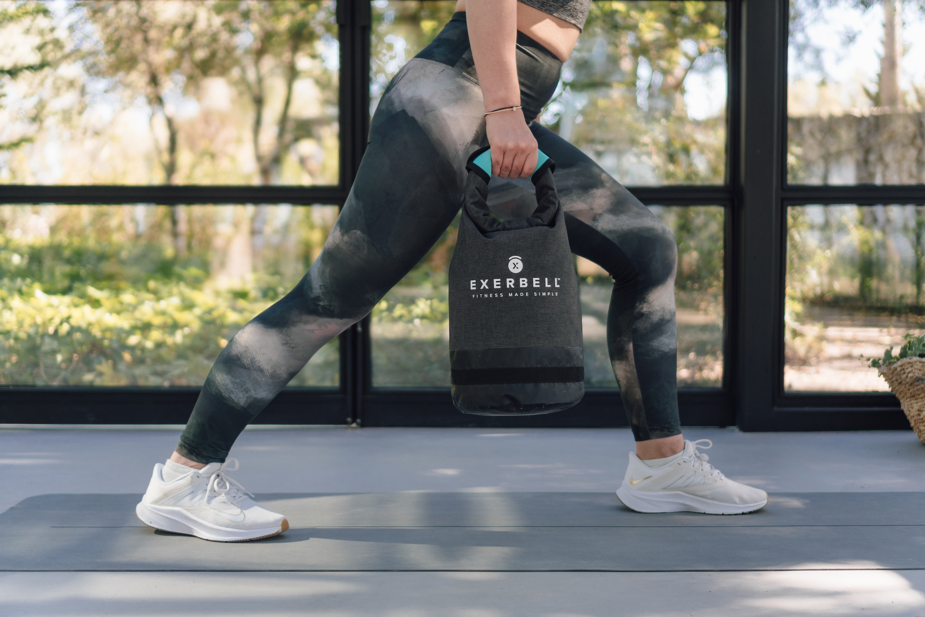 Femme en tenue de sport tenant un poids Exerbell gris en position de fente.