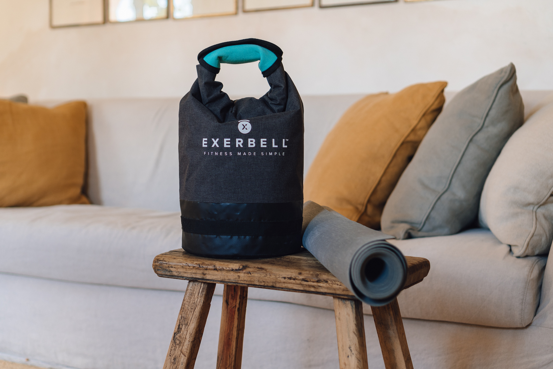 Un sac de fitness gris avec une poignée turquoise est sur un tabouret en bois à côté d'un tapis de yoga roulé.
