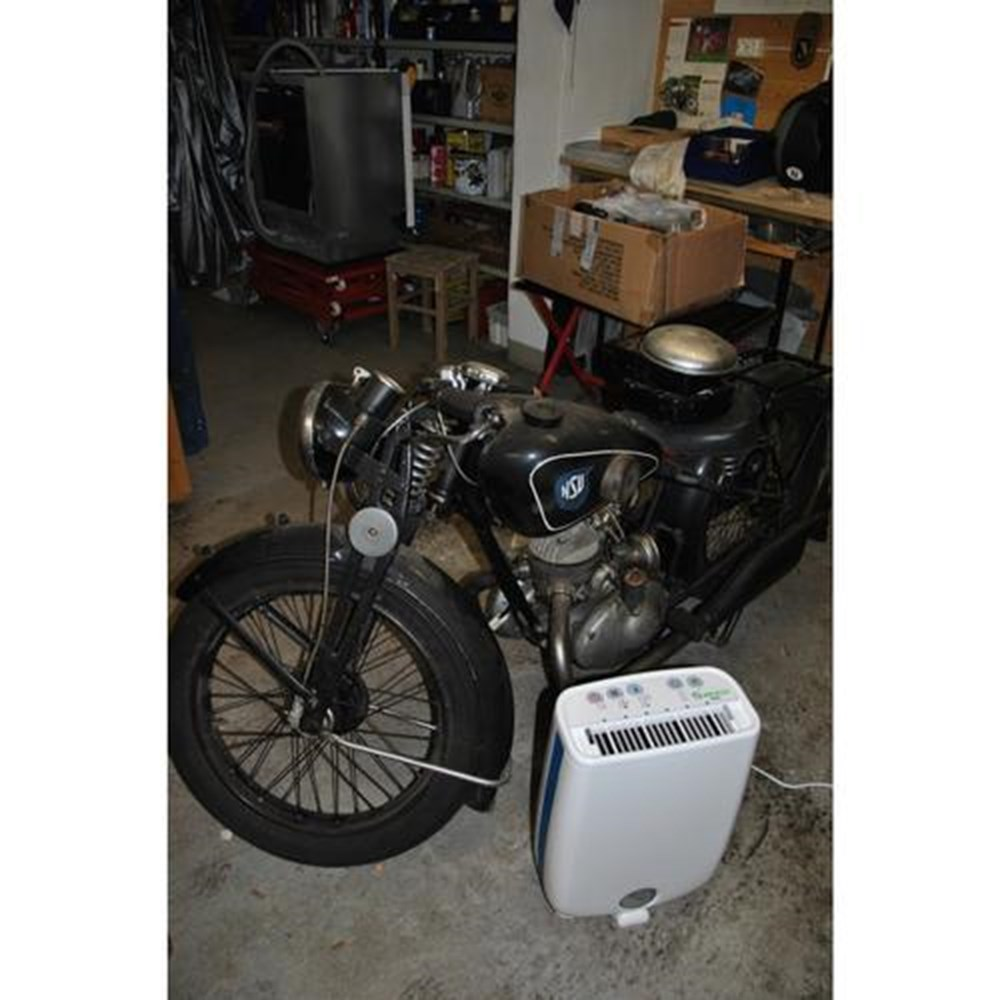 Een zwarte motor staat naast een witte luchtontvochtiger in een garage.