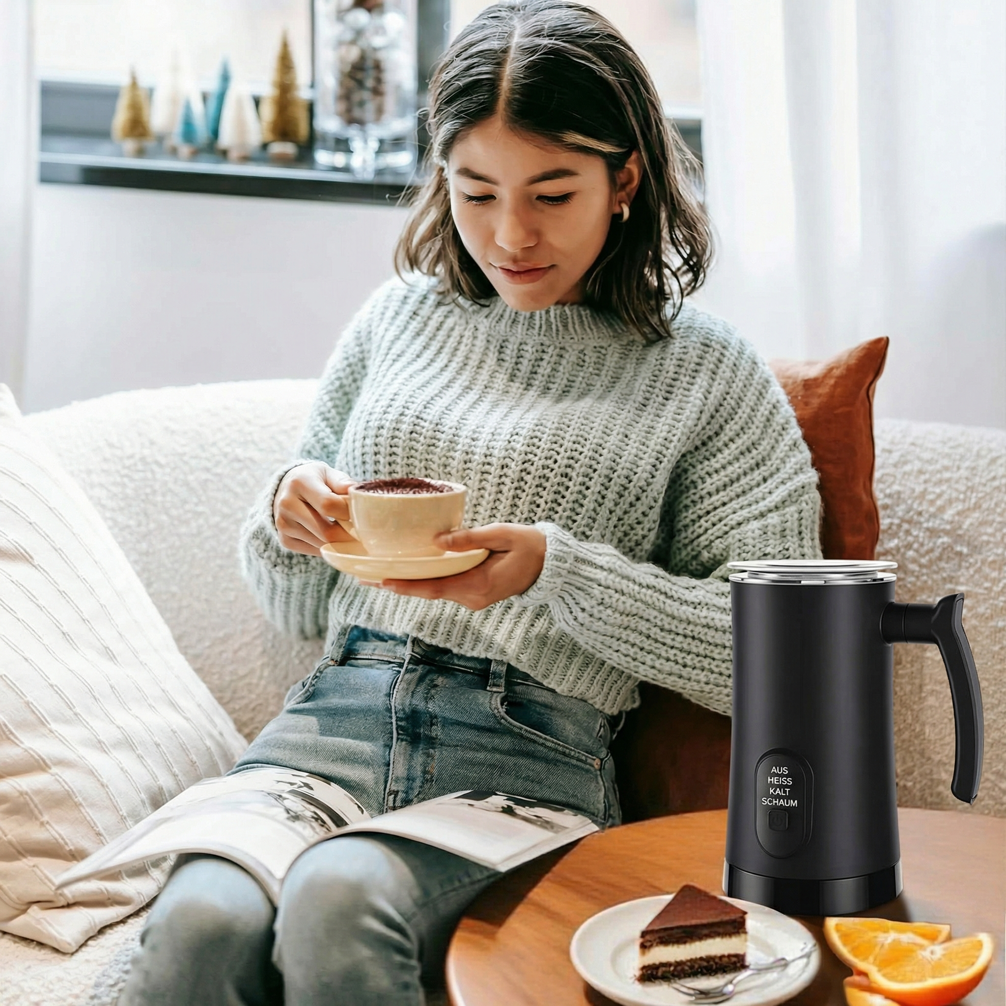 Eine Frau sitzt auf einer Couch und trinkt Kaffee. Ein Milchaufschäumer steht daneben.