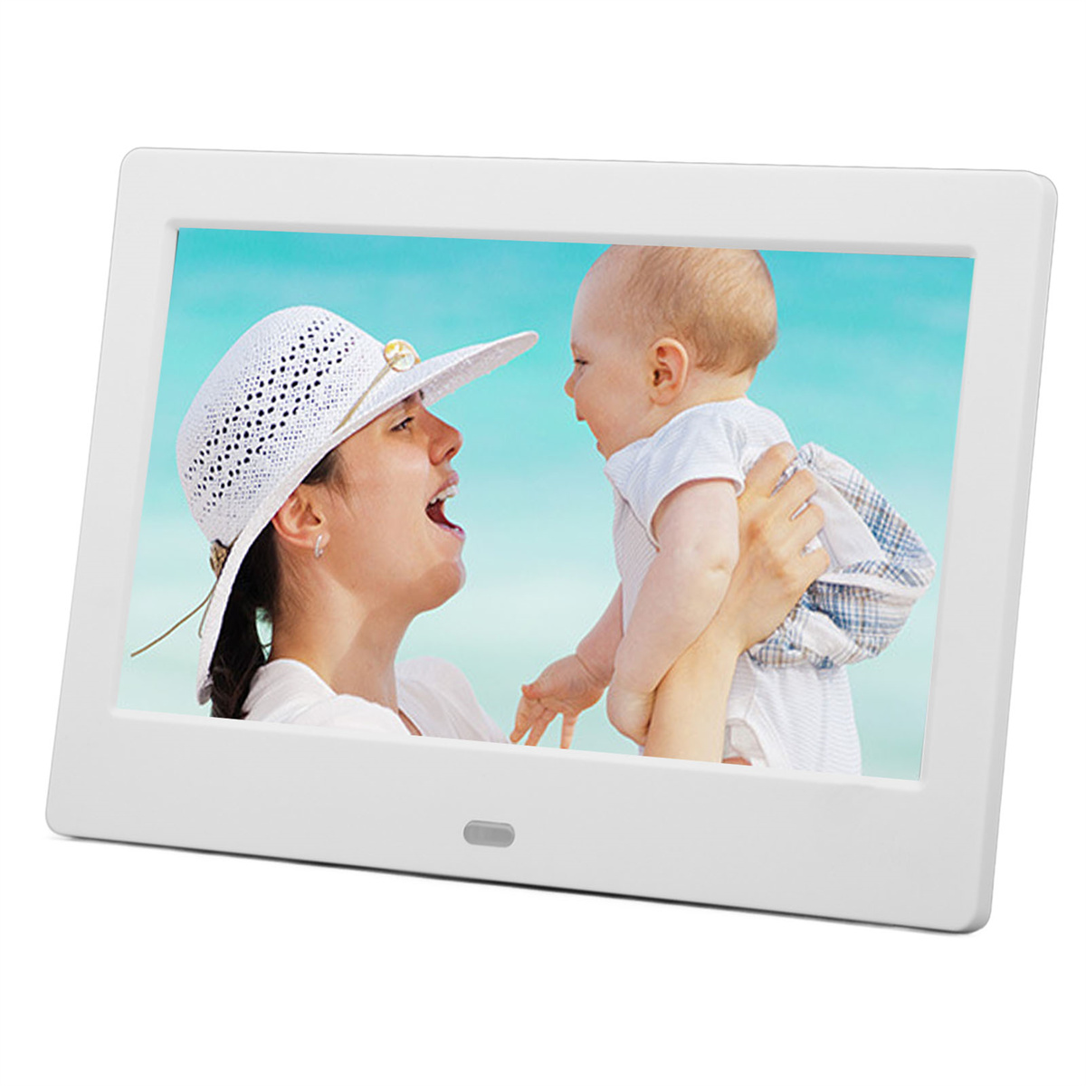Mutter mit Hut hält Baby am Strand vor blauem Meer.