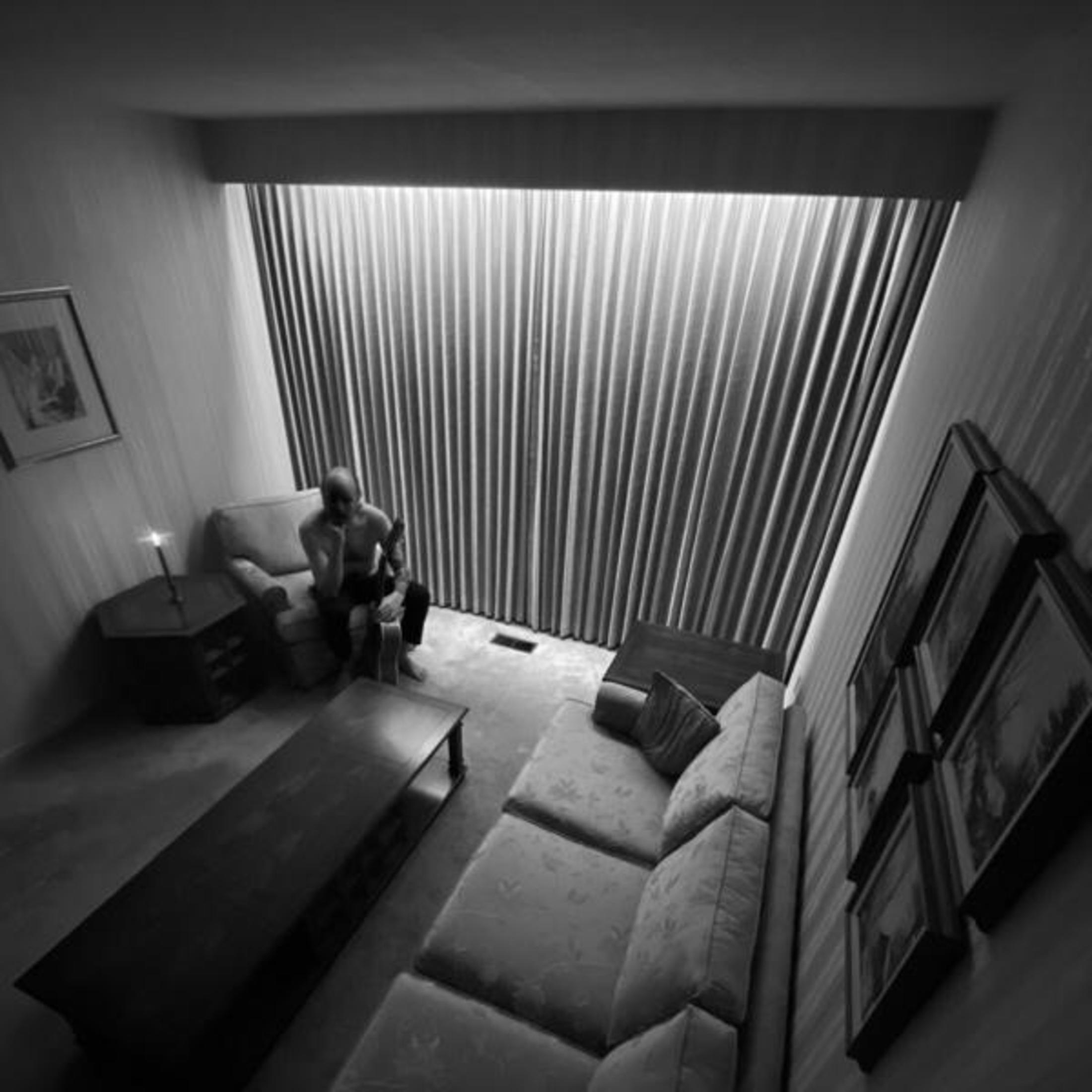 Un uomo siede pensieroso in una stanza poco illuminata con tende.