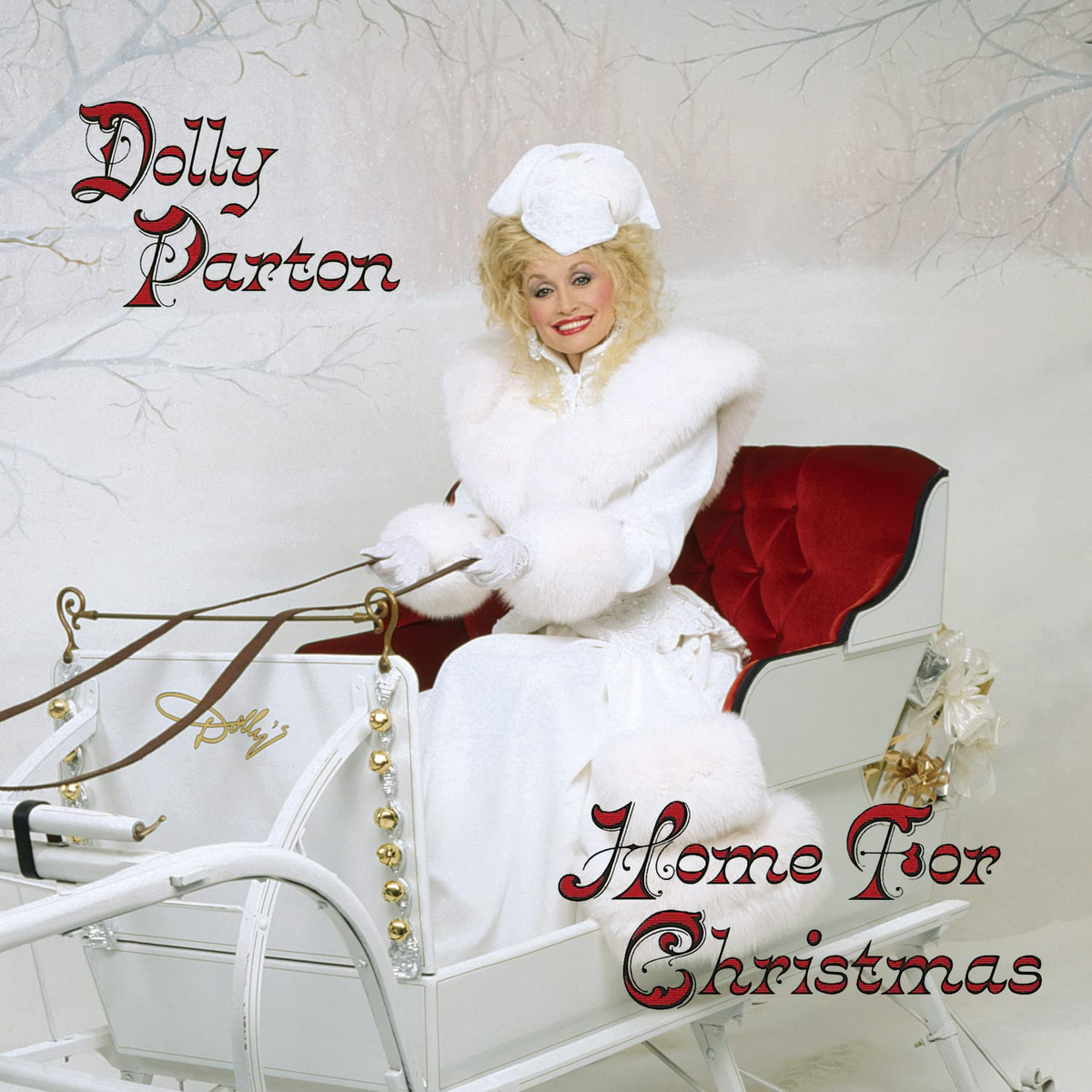 Dolly Parton in un cappotto di pelliccia bianco siede su una slitta nella neve.