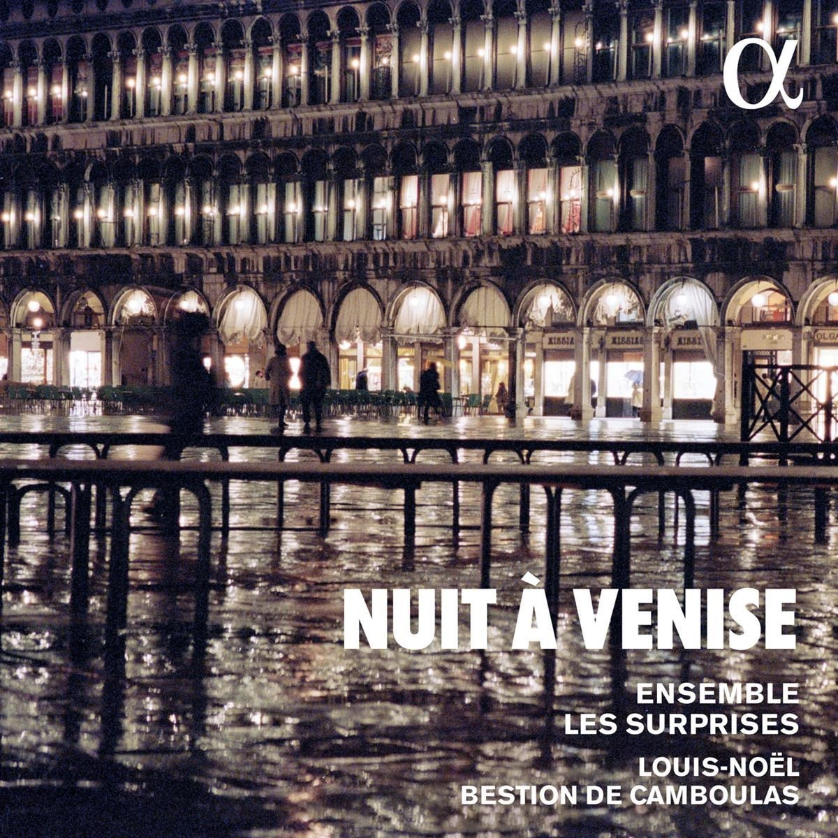 Notte a Venezia: arcate illuminate e riflessi su una piazza bagnata.