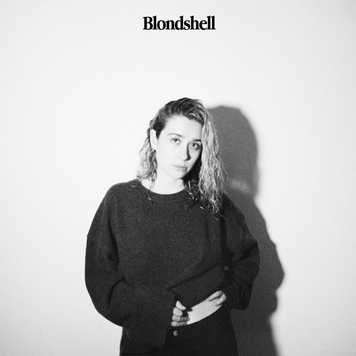Logo Blondshell sopra una donna in maglione scuro su muro bianco.