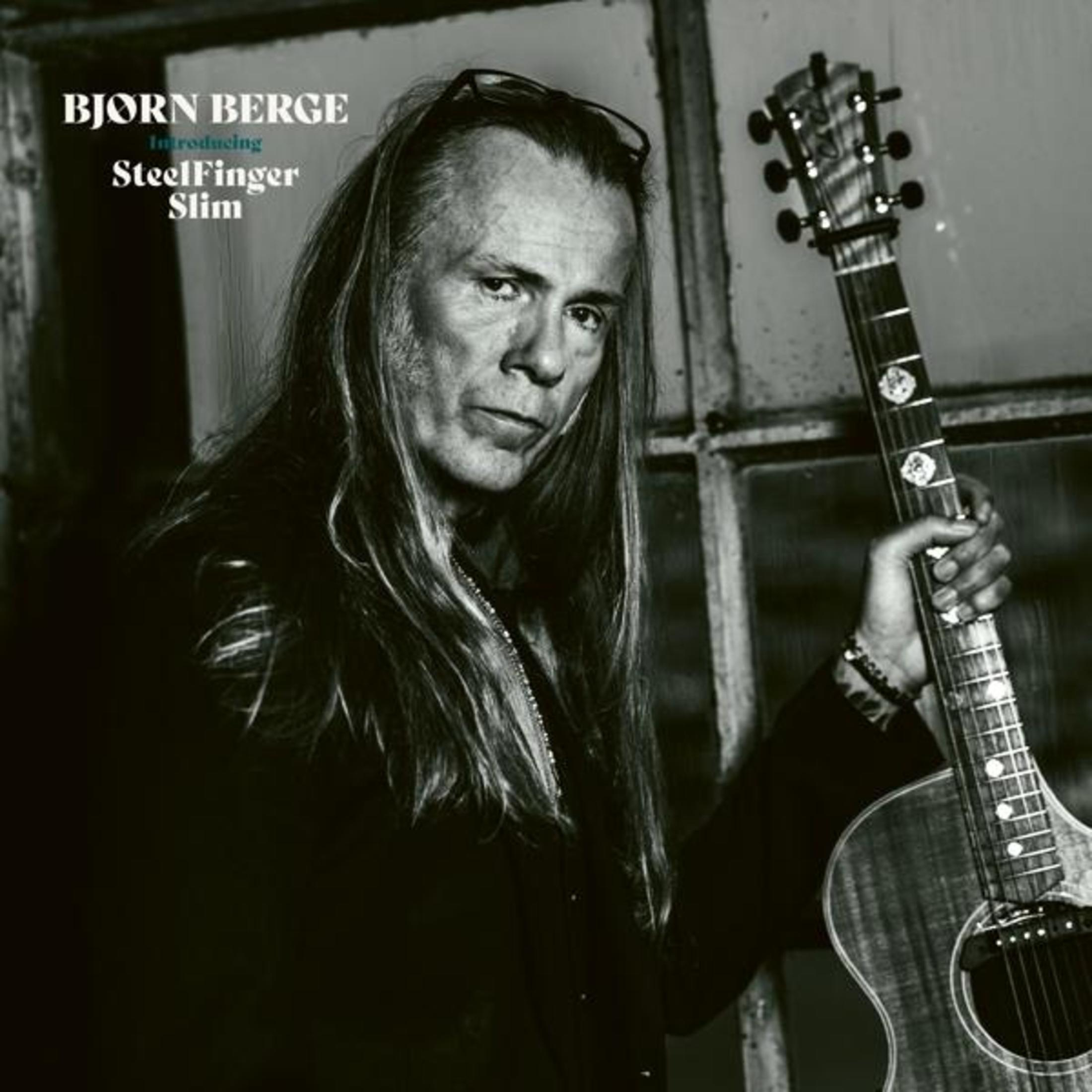Uomo con capelli lunghi tiene chitarra. Björn Berge Presenta SteelFinger Slim.