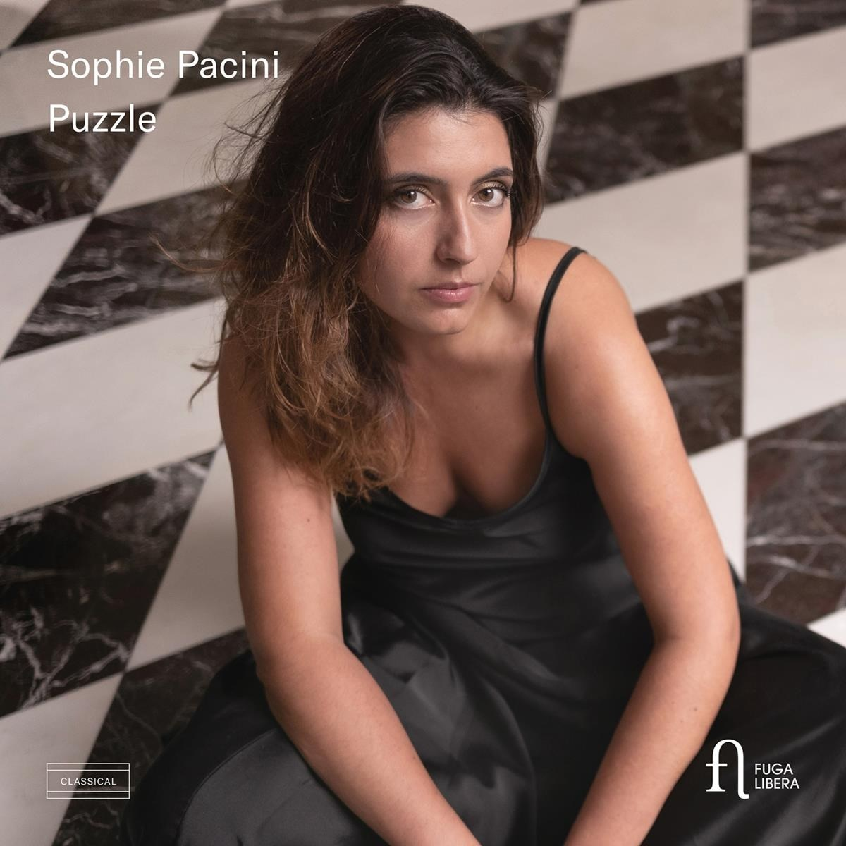 Donna con capelli castani in abito nero seduta davanti a muro a scacchi.