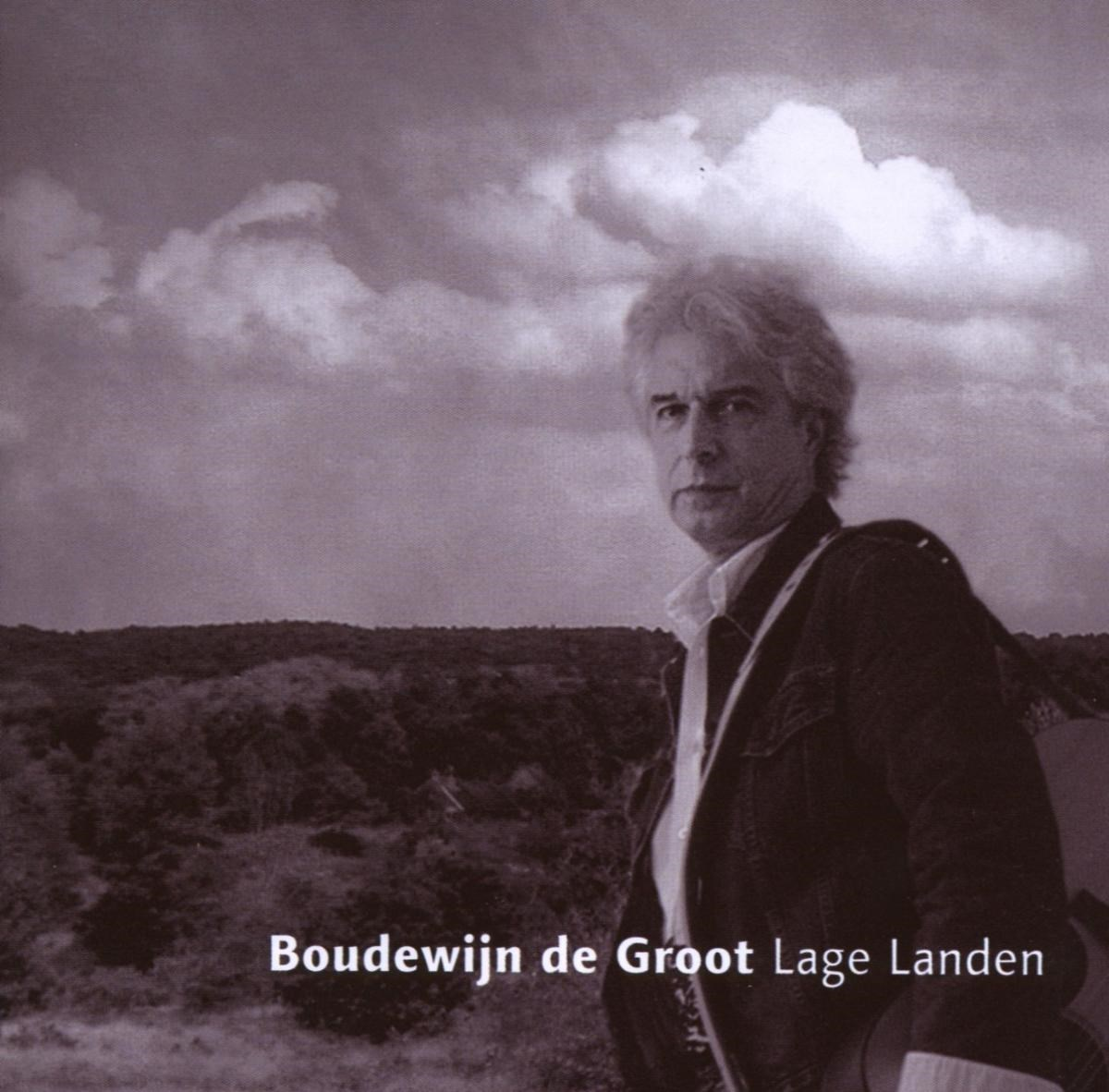 Een man met grijs haar staat voor een heuvelachtig landschap en wolken.