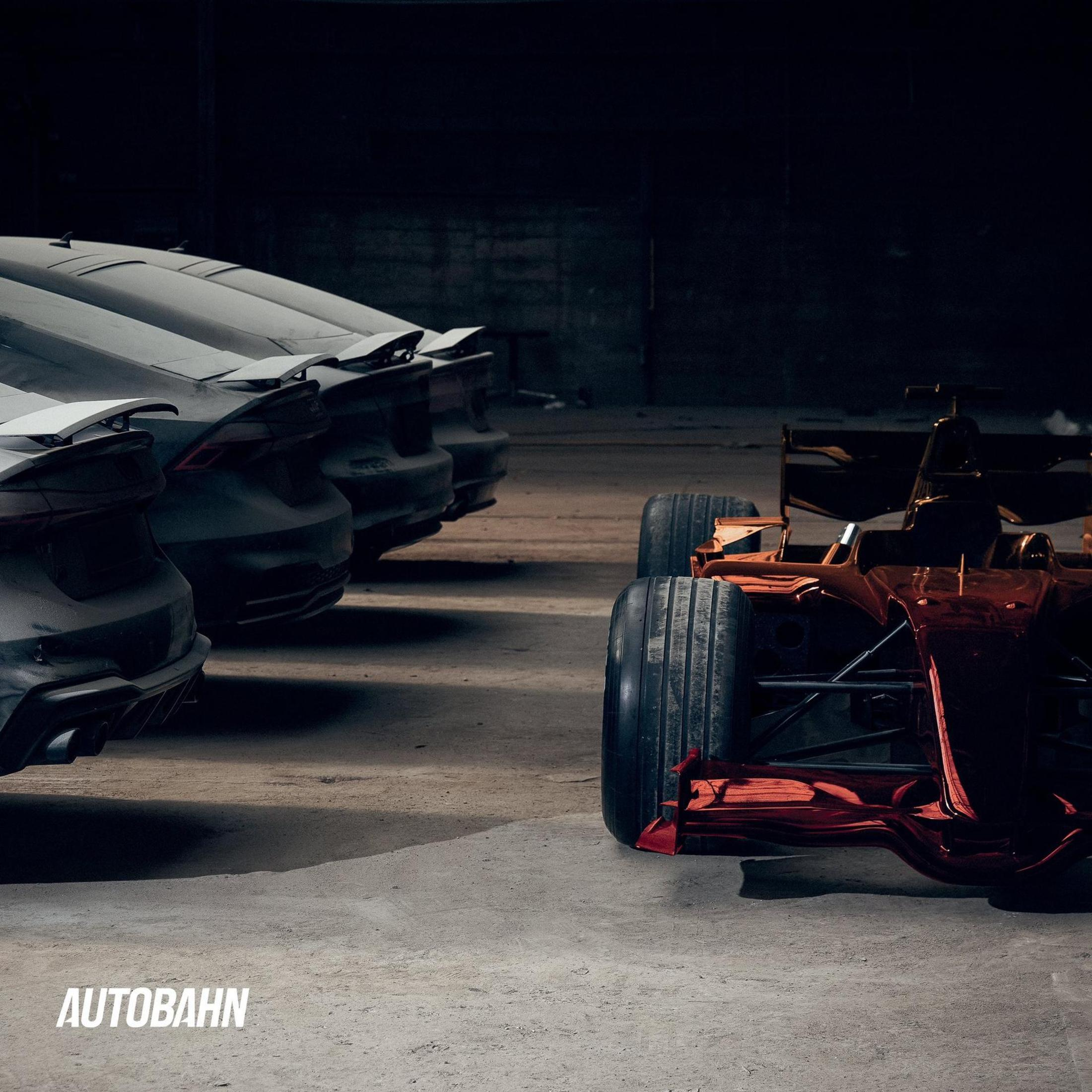 Un'auto di Formula 1 rossa parcheggiata accanto a una fila di auto scure in un garage.