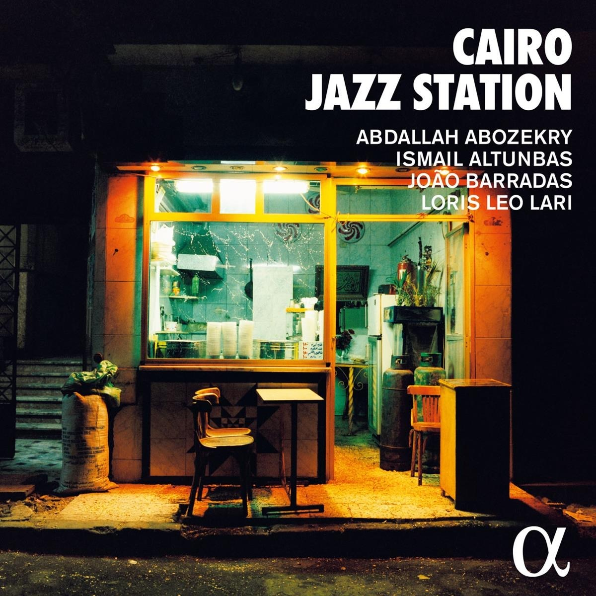 Una stazione jazz al Cairo di notte, con una vetrina illuminata, sedie e tavolo.
