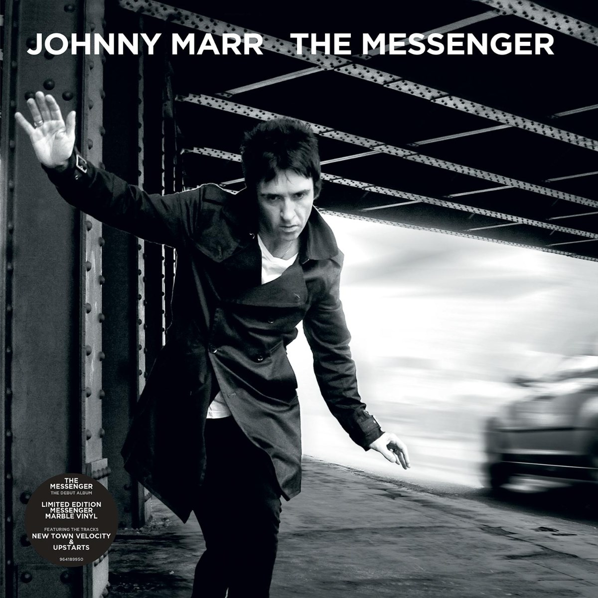 Johnny Marr in piedi sotto un ponte, un'auto sfocata sullo sfondo.