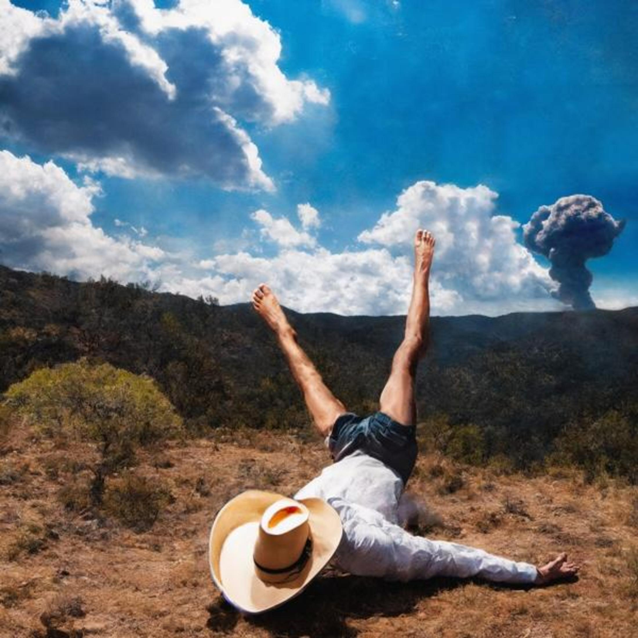 Uomo a terra, piedi in aria, cappello nelle vicinanze, pennacchio di fumo nel cielo.