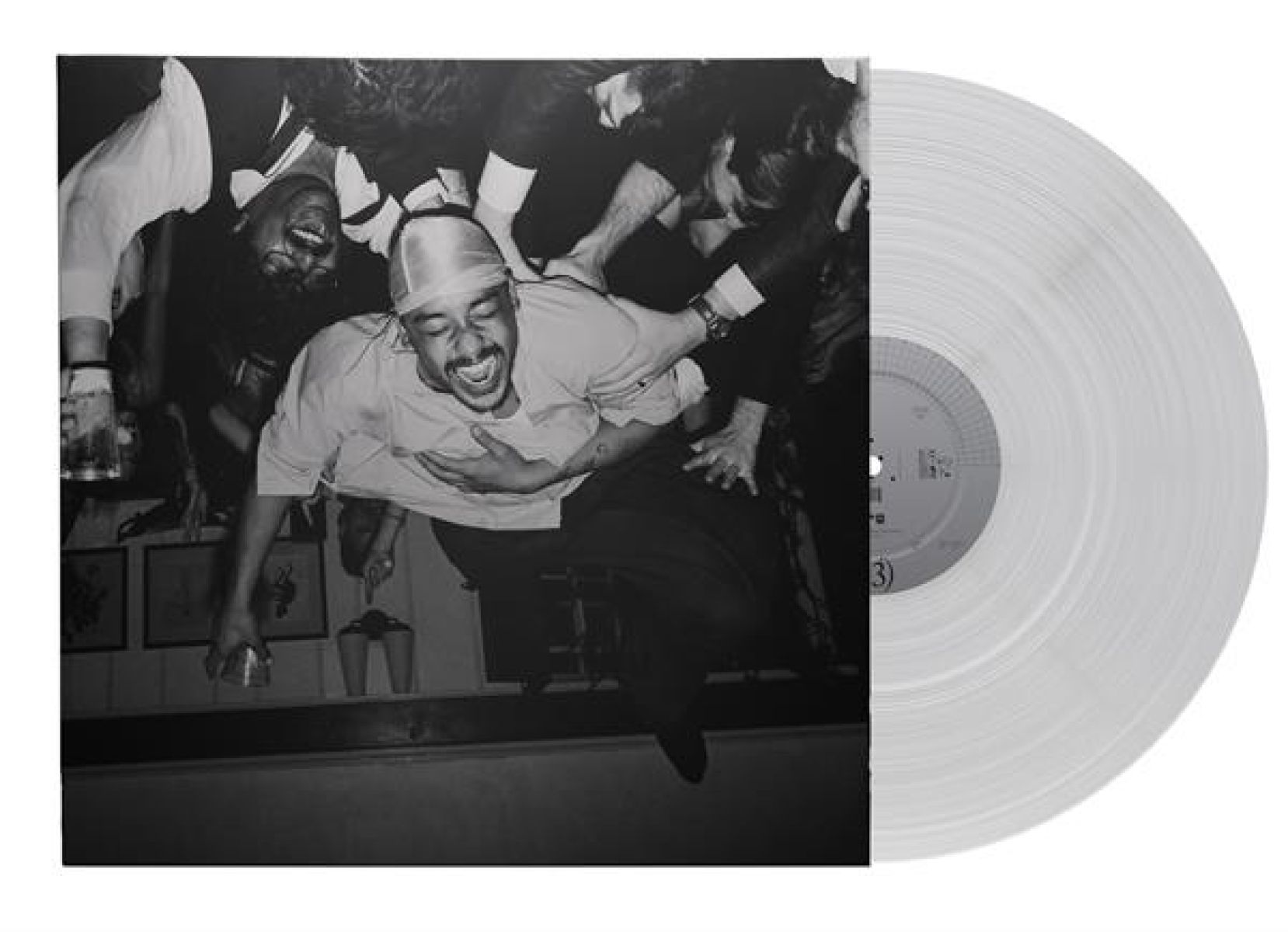 Un uomo con durag ride mentre altri lo abbracciano dall'alto. Un disco in vinile accanto.