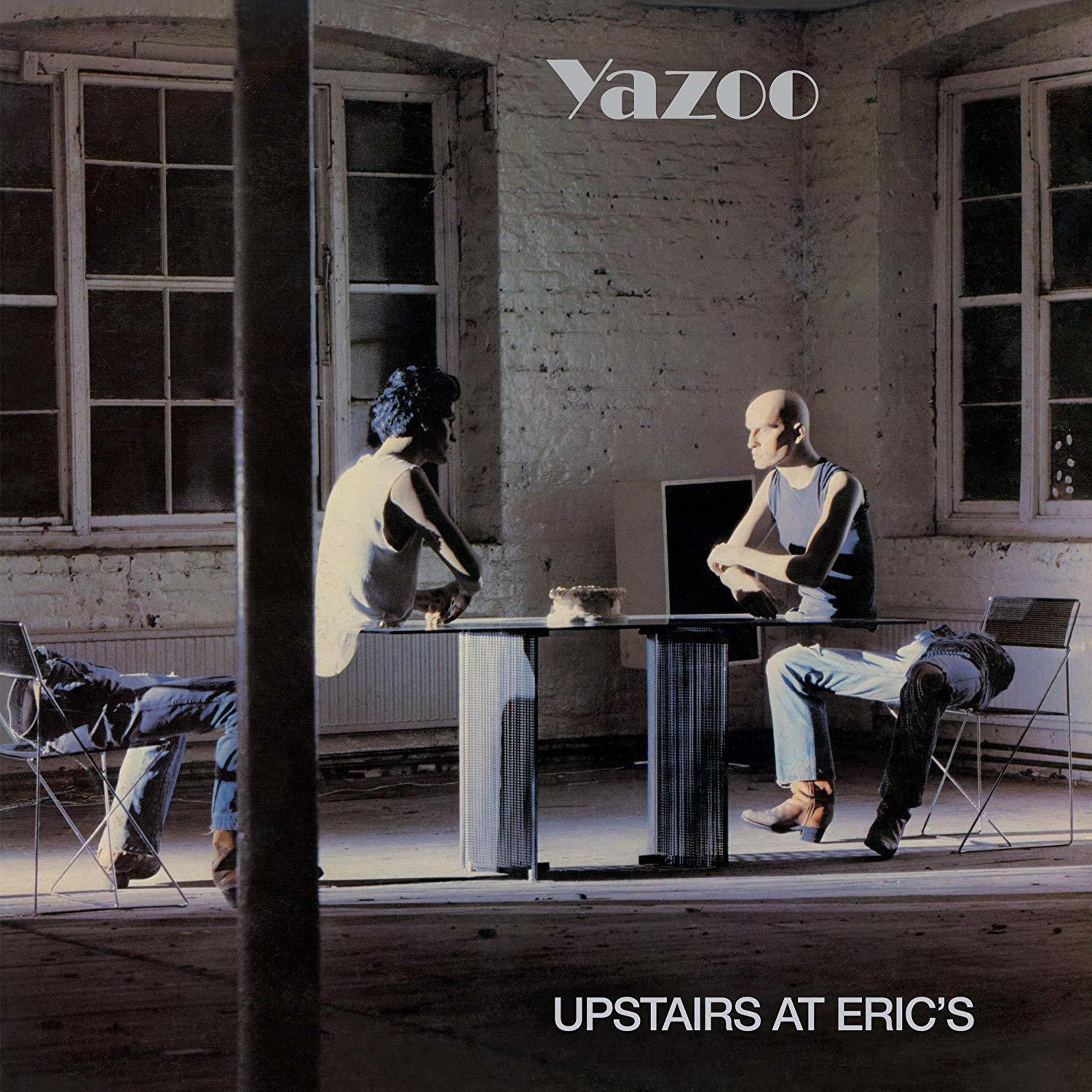 Due uomini seduti a un tavolo in una stanza con finestre. Sono visibili "Yazoo" e "Upstairs at Eric's".