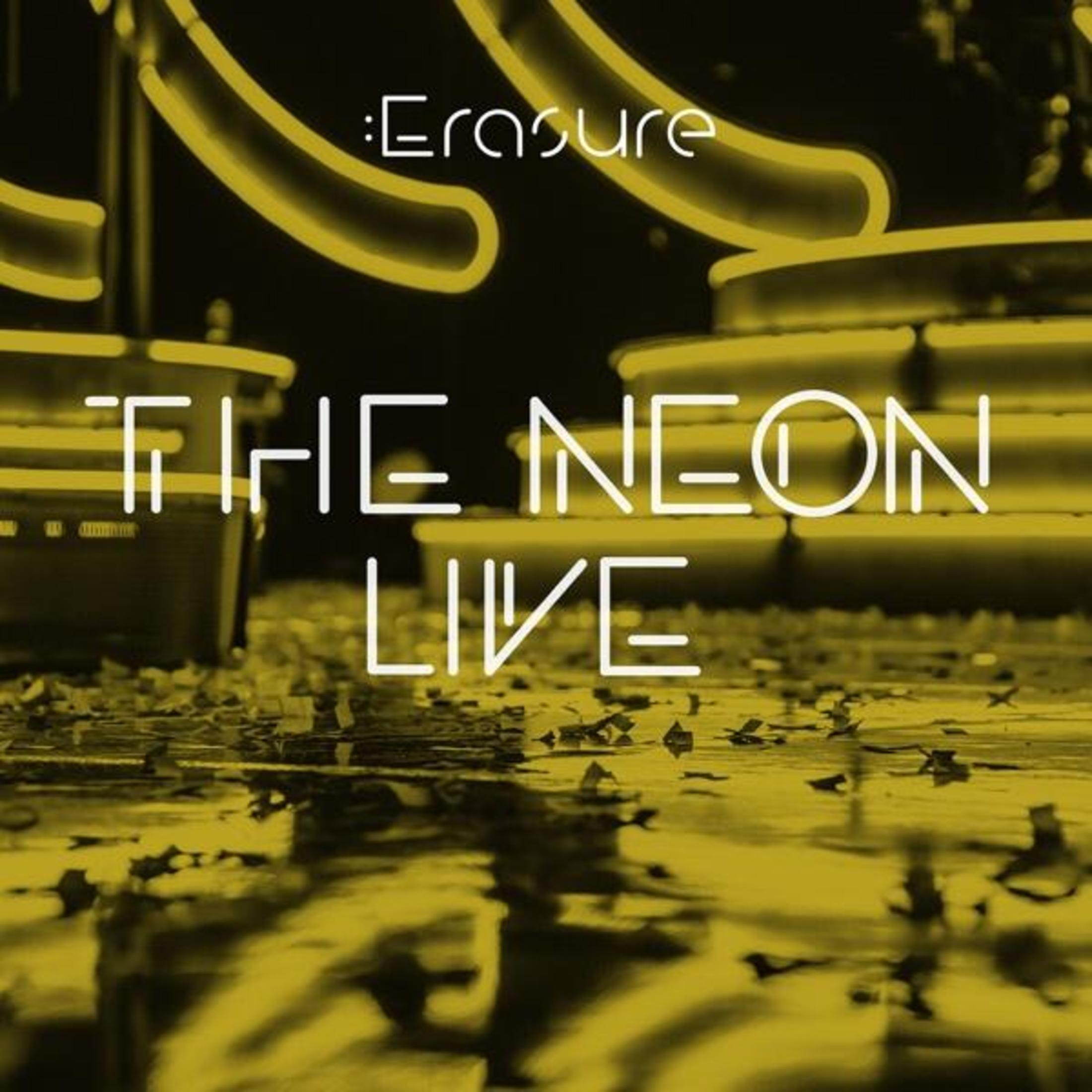 Testo al neon giallo "Erasure The Neon Live" su sfondo nero con pavimento riflettente.