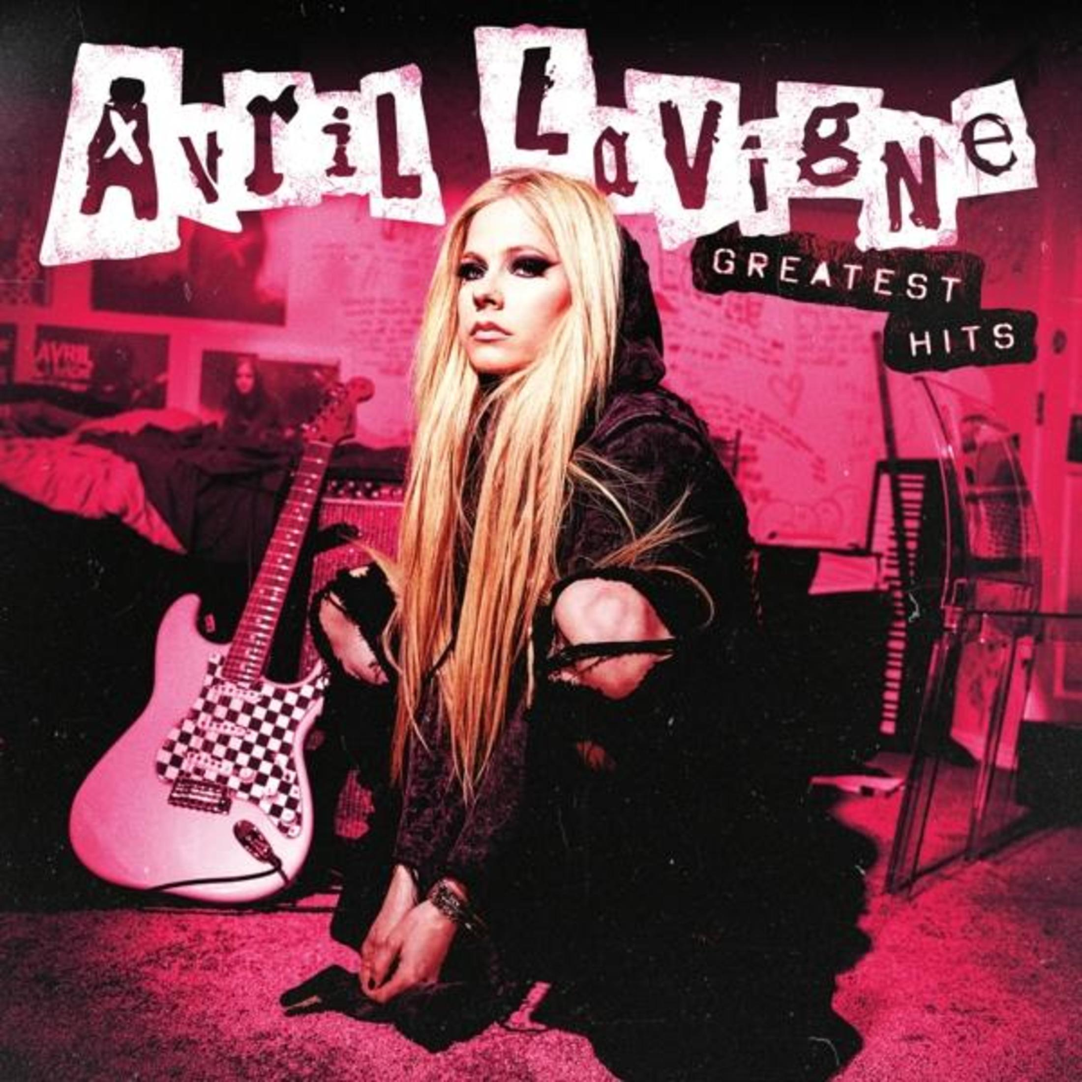 Avril Lavigne siede con chitarra e amplificatore davanti a un suo poster.