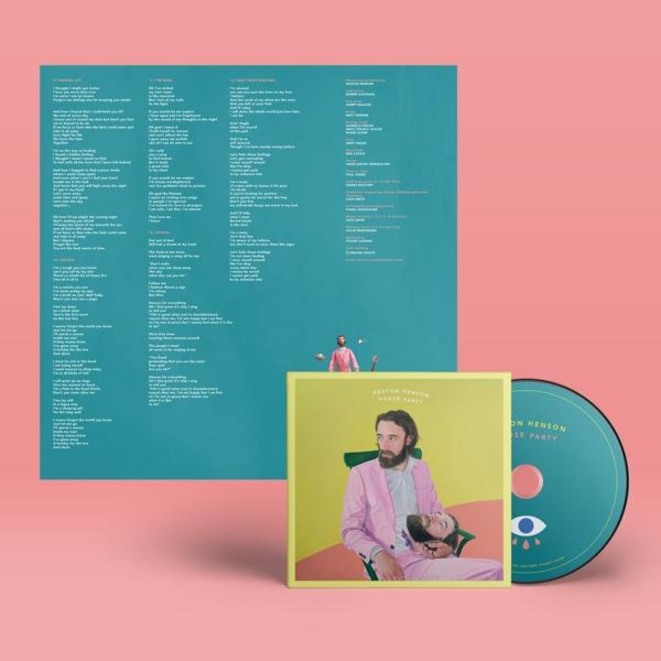Un uomo in completo rosa è seduto, tiene un altro uomo. Vinile e CD accanto.