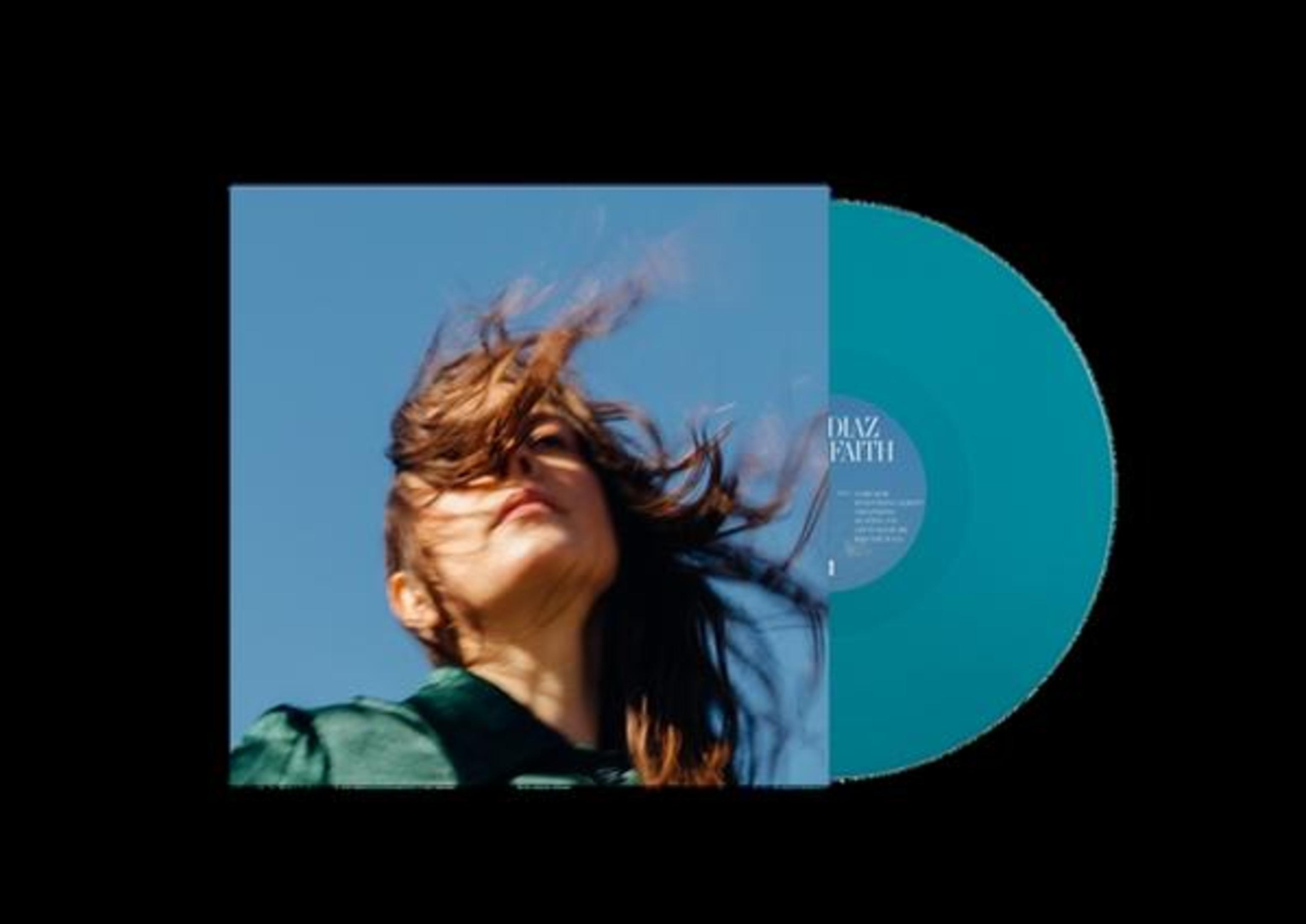 Donna guarda in alto, capelli al vento, cielo blu, accanto un disco in vinile blu.