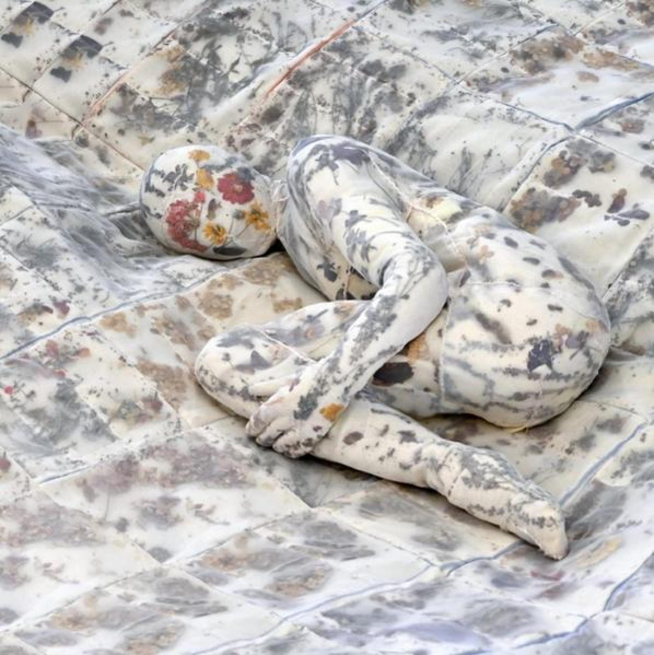 Una bambola di stoffa giace su una coperta fantasia. Grigio e bianco.