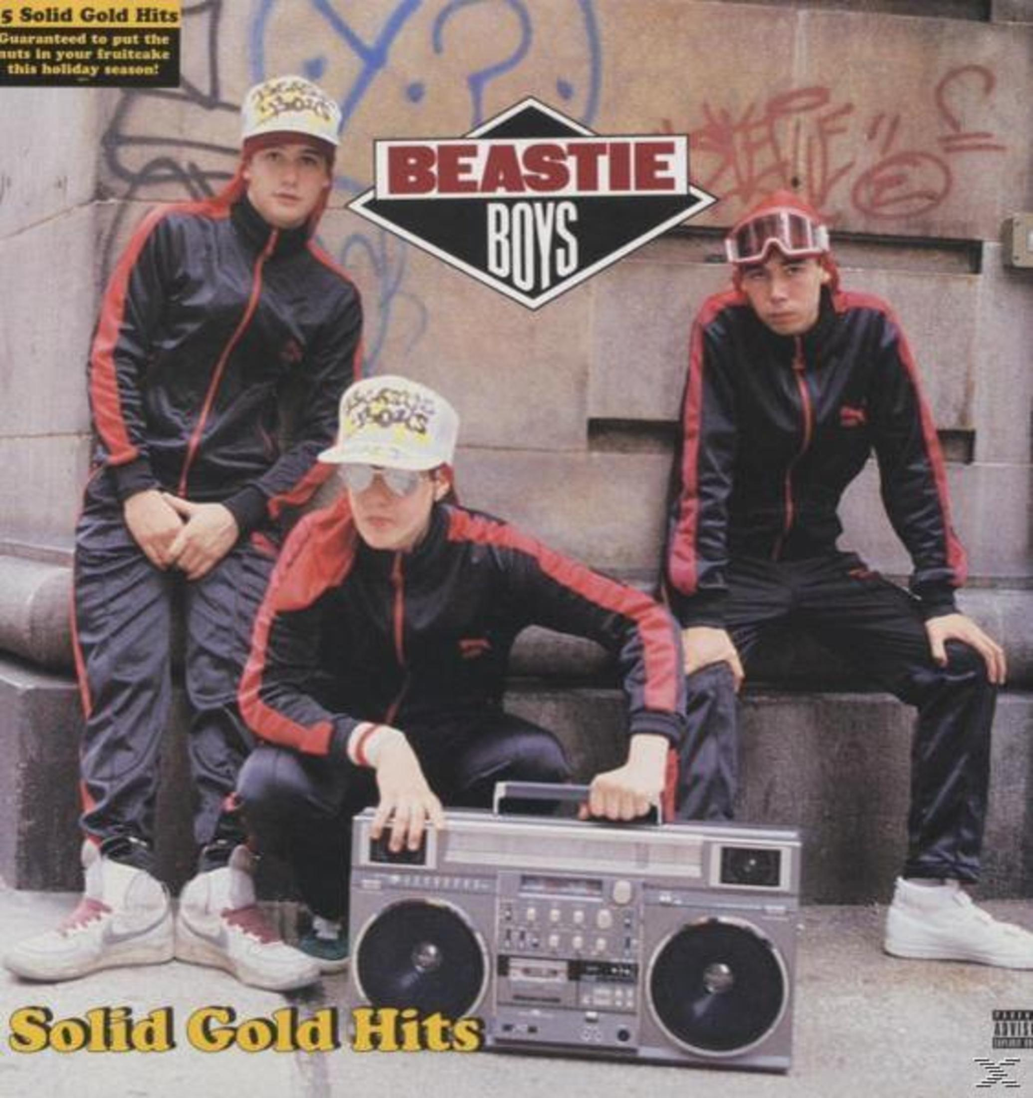Tre uomini in tuta posano con un boombox davanti a un muro con graffiti.